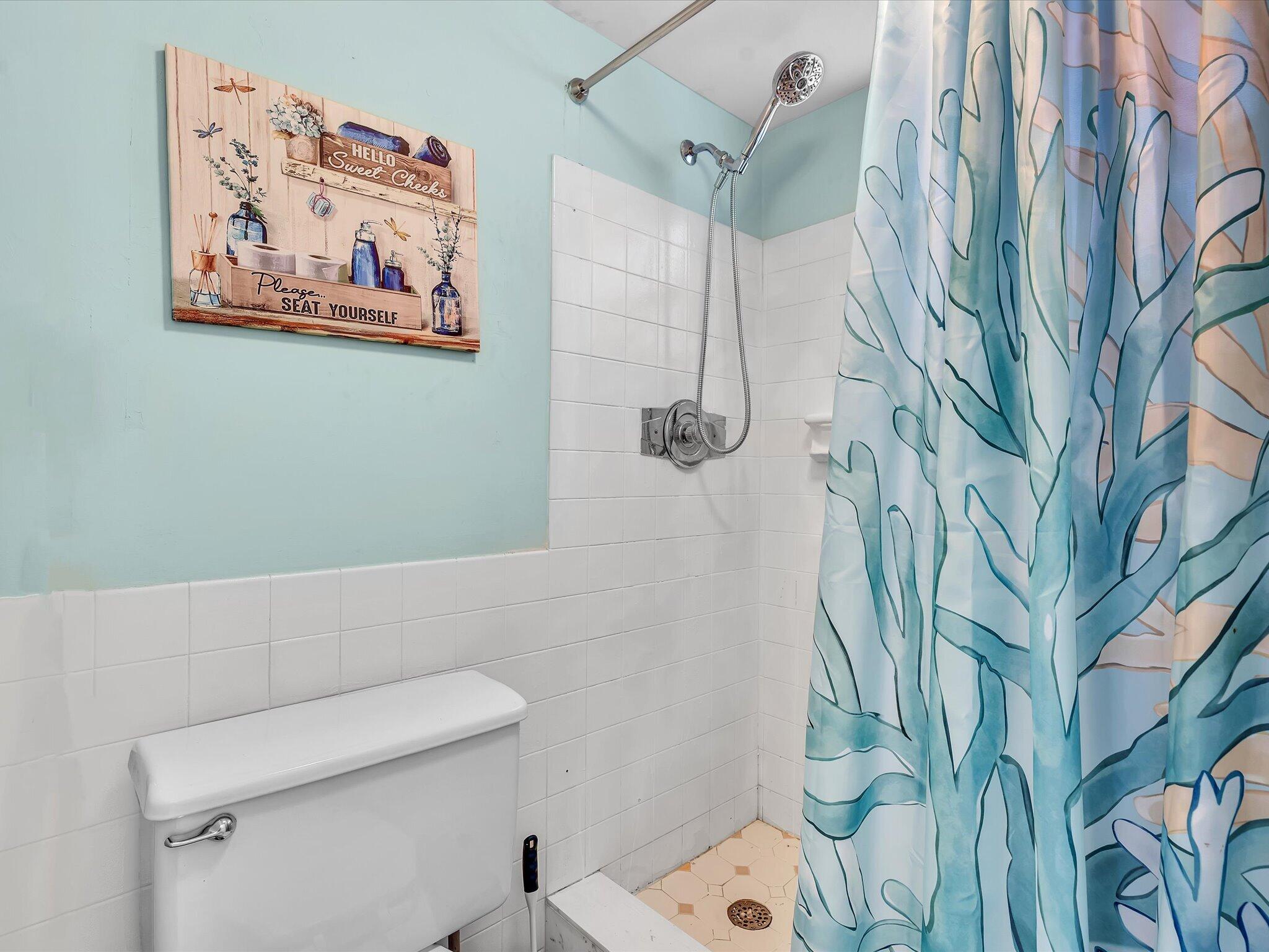 Bathroom shower with a blue patterned curtain, white tile, and a decorative sign above the toilet.