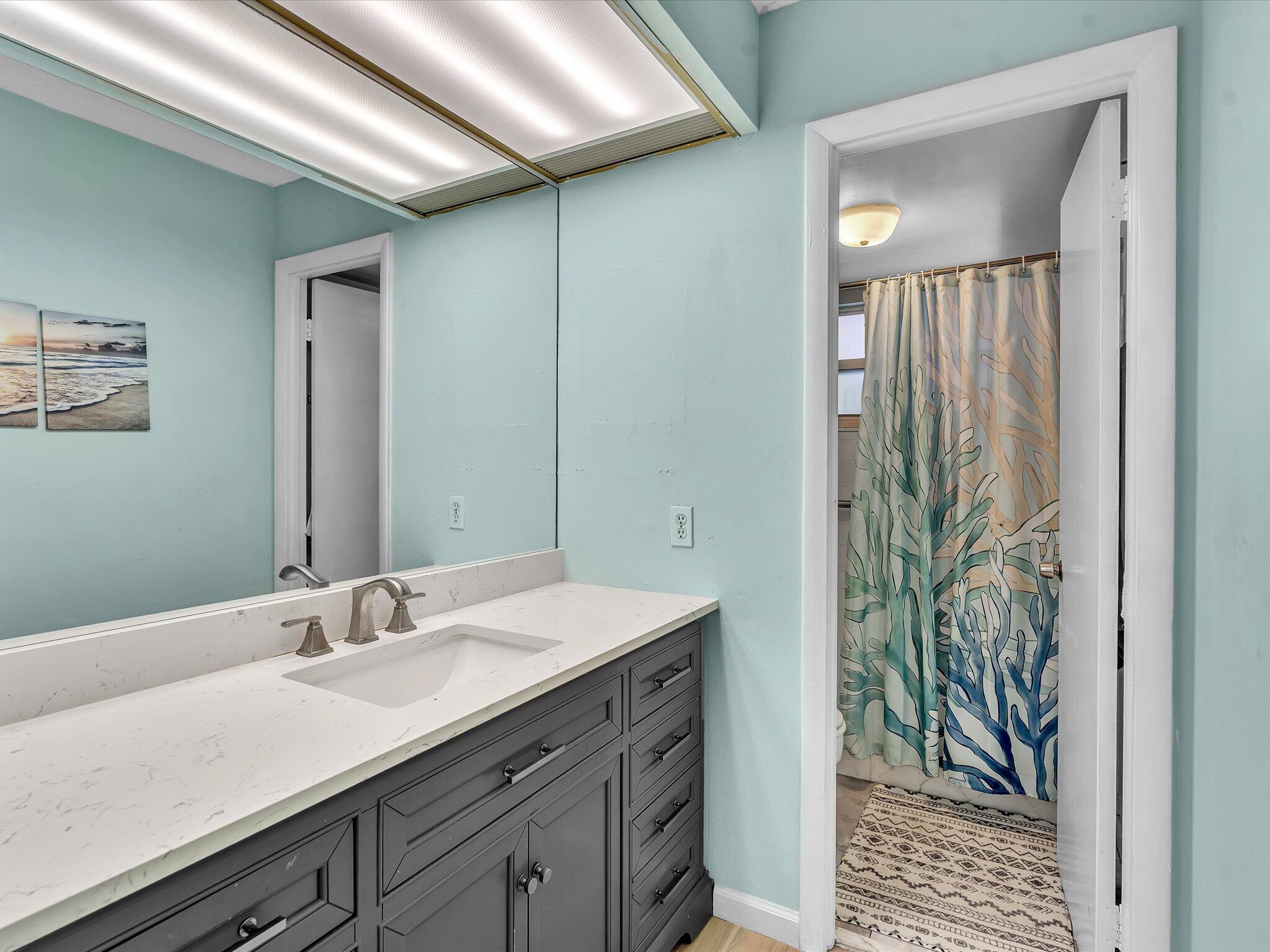 Bathroom with a dark gray vanity, white countertop, aqua walls, and patterned shower curtain.