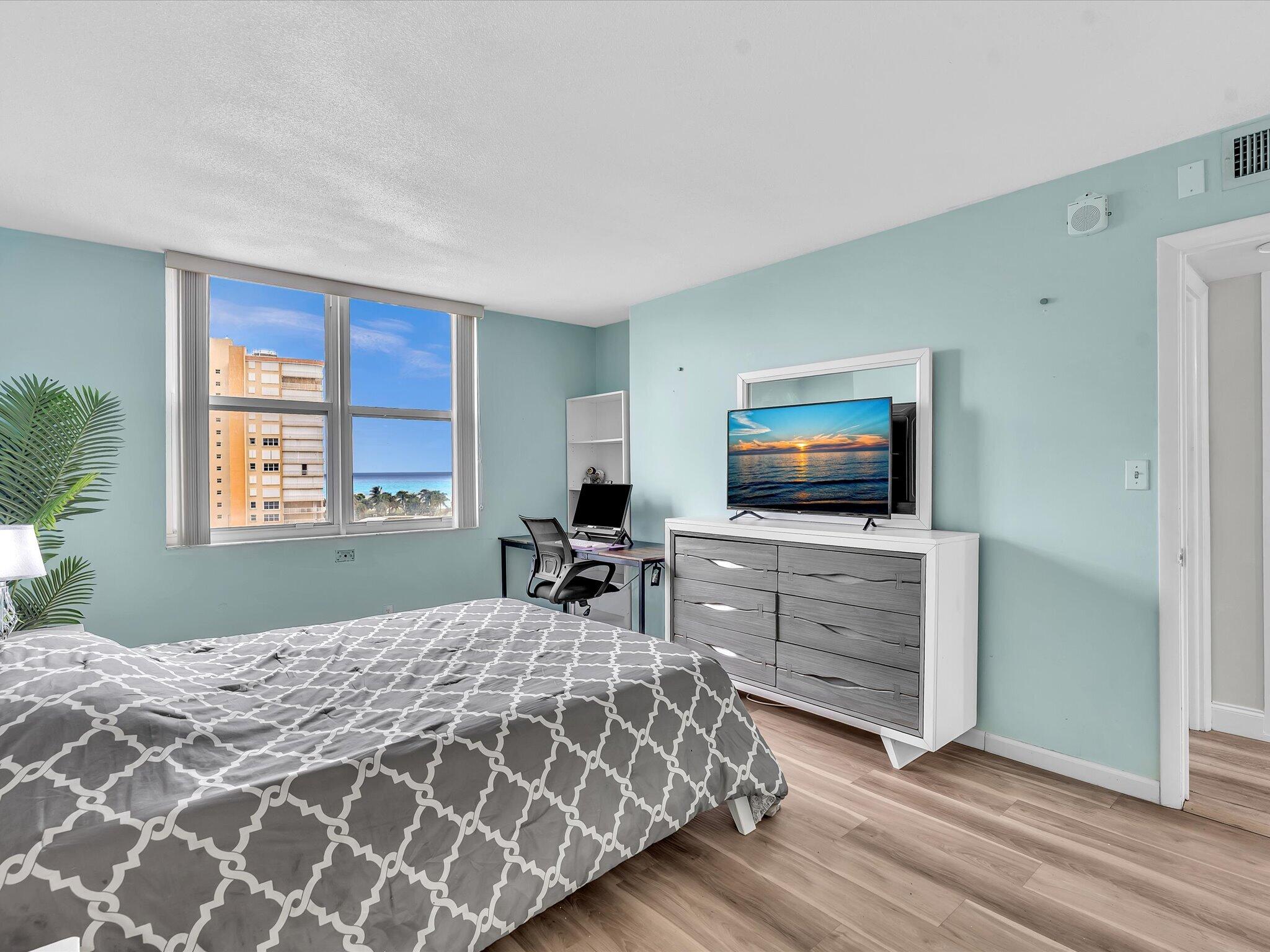 Bedroom with a gray patterned bed and ocean view through the window.