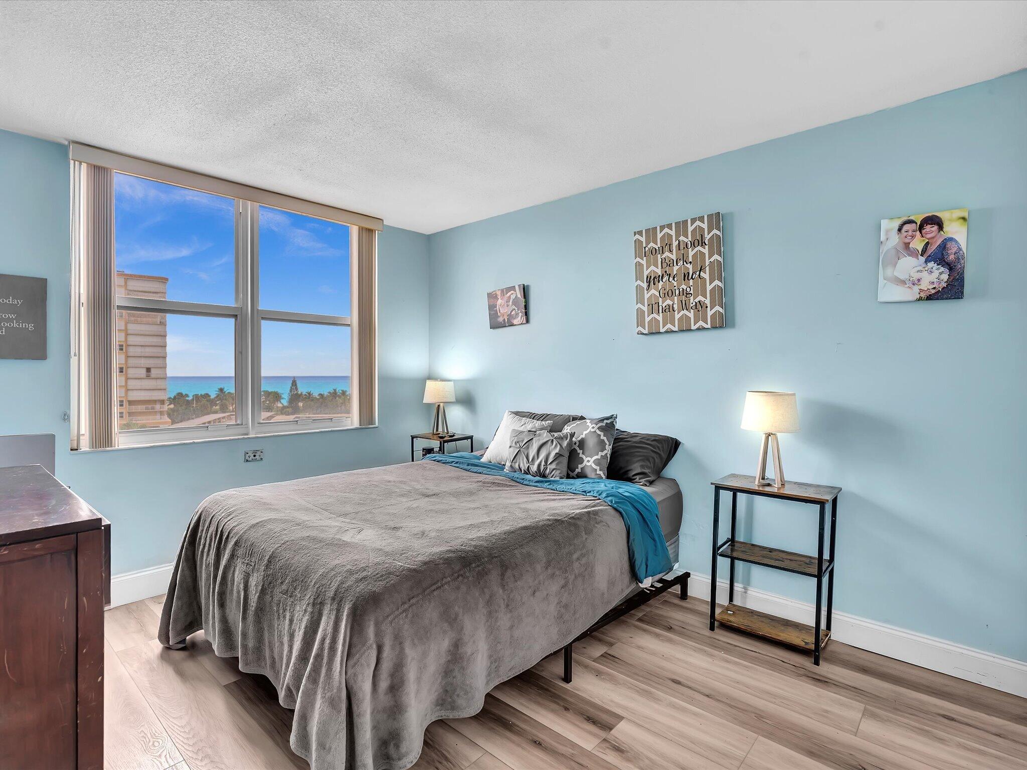 Furnished bedroom with a gray-covered bed and ocean view through a large window.