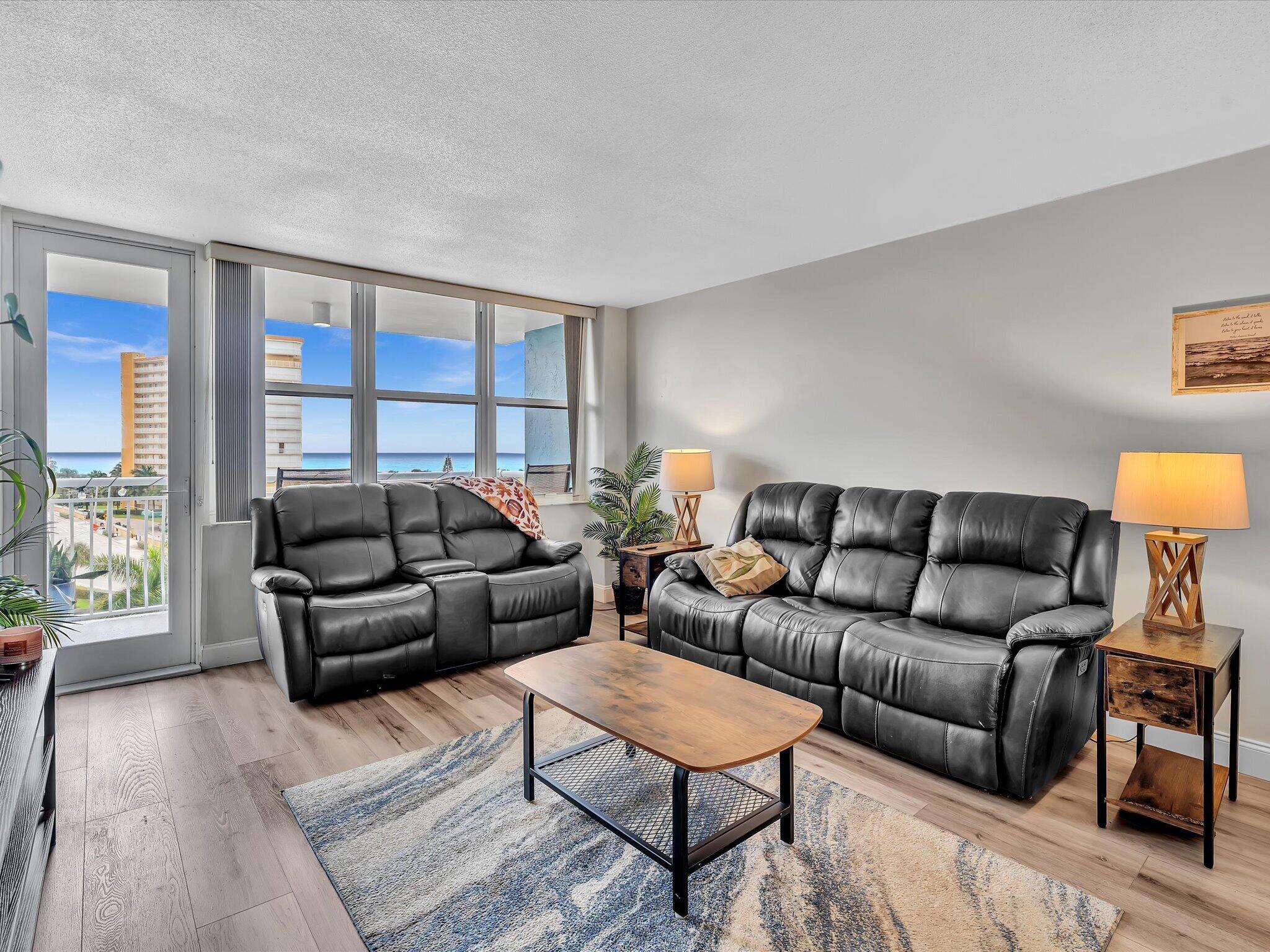 Living room with black leather sofas and ocean views through large windows.