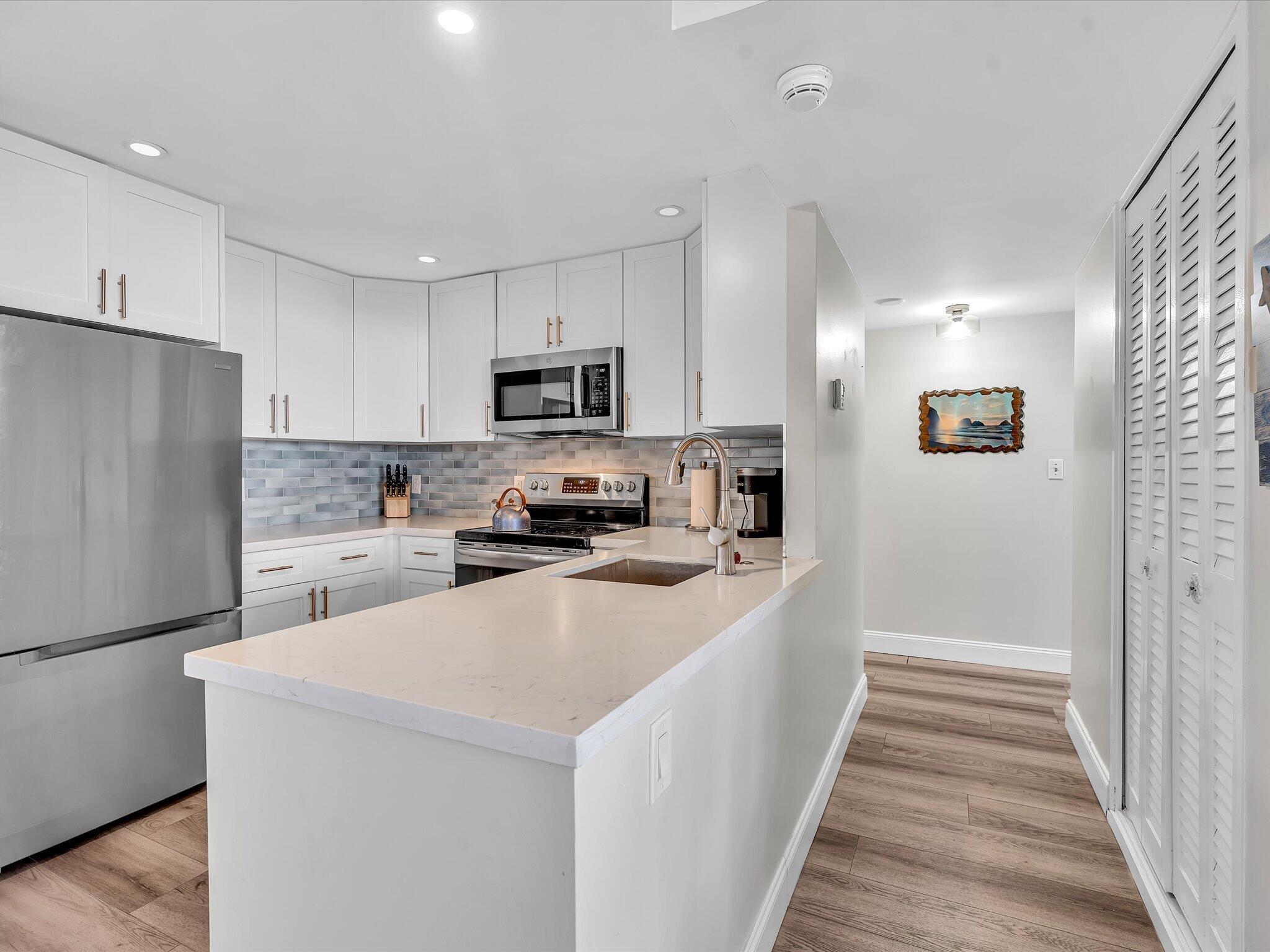 Kitchen with white cabinets, stainless steel appliances, gray tile backsplash, and a large peninsula sink.