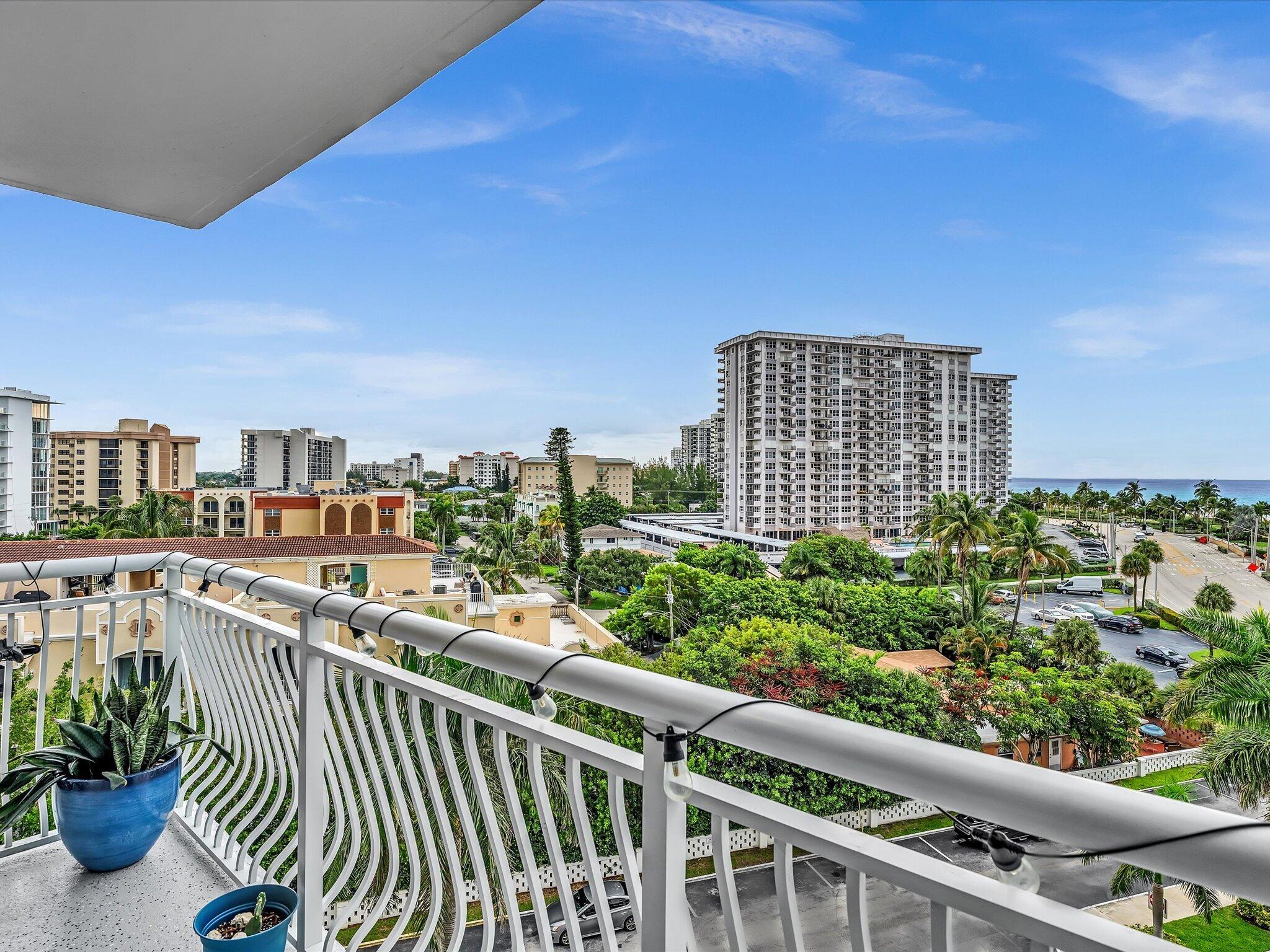 High-rise balcony overlooking palm trees, coastal buildings, and the ocean.