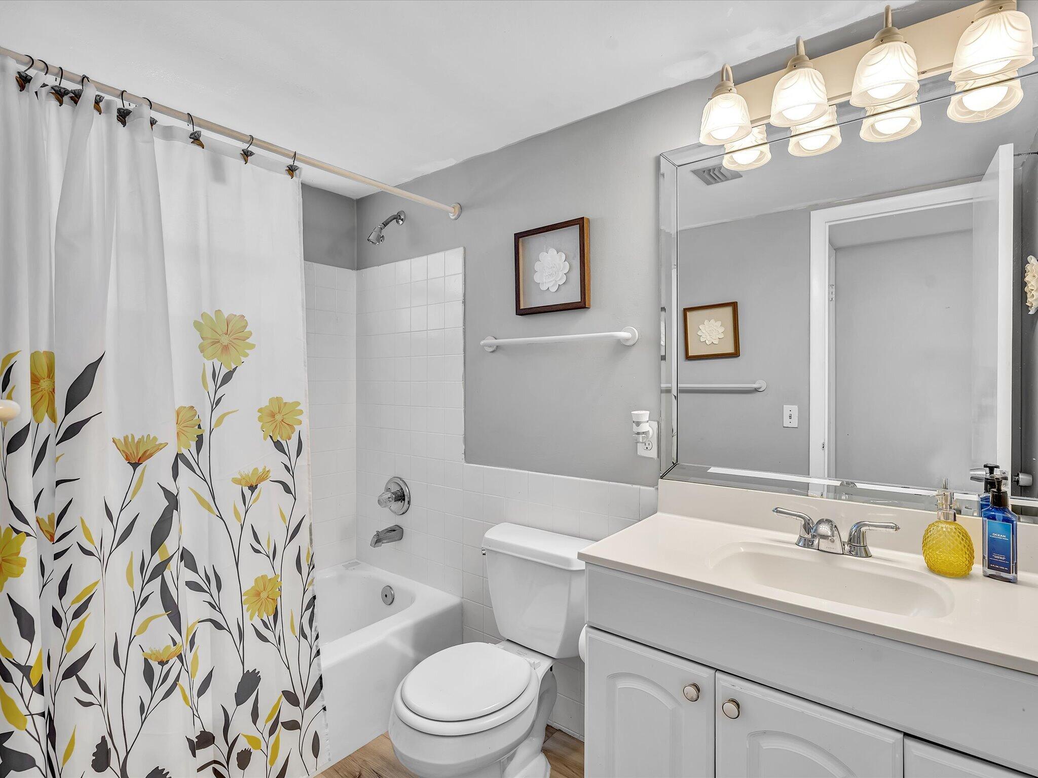 Bathroom with a yellow-flower shower curtain, white tub, and vanity beneath a large mirror.