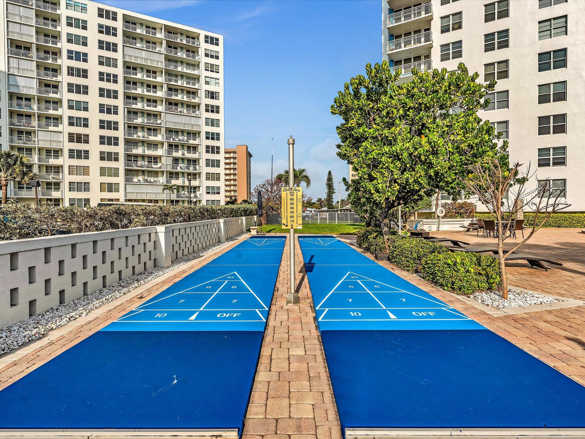 Blue shuffleboard courts between condominium towers, with landscaped grounds and patio seating.