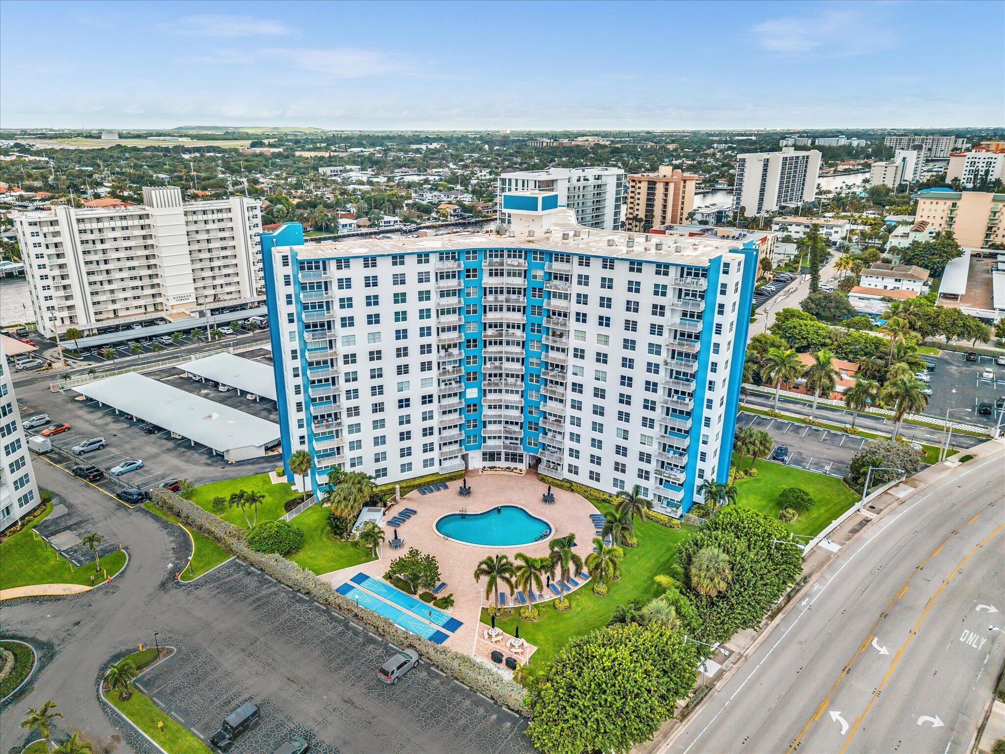 White-and-blue high-rise condominium with a courtyard pool and tennis court, viewed from above.