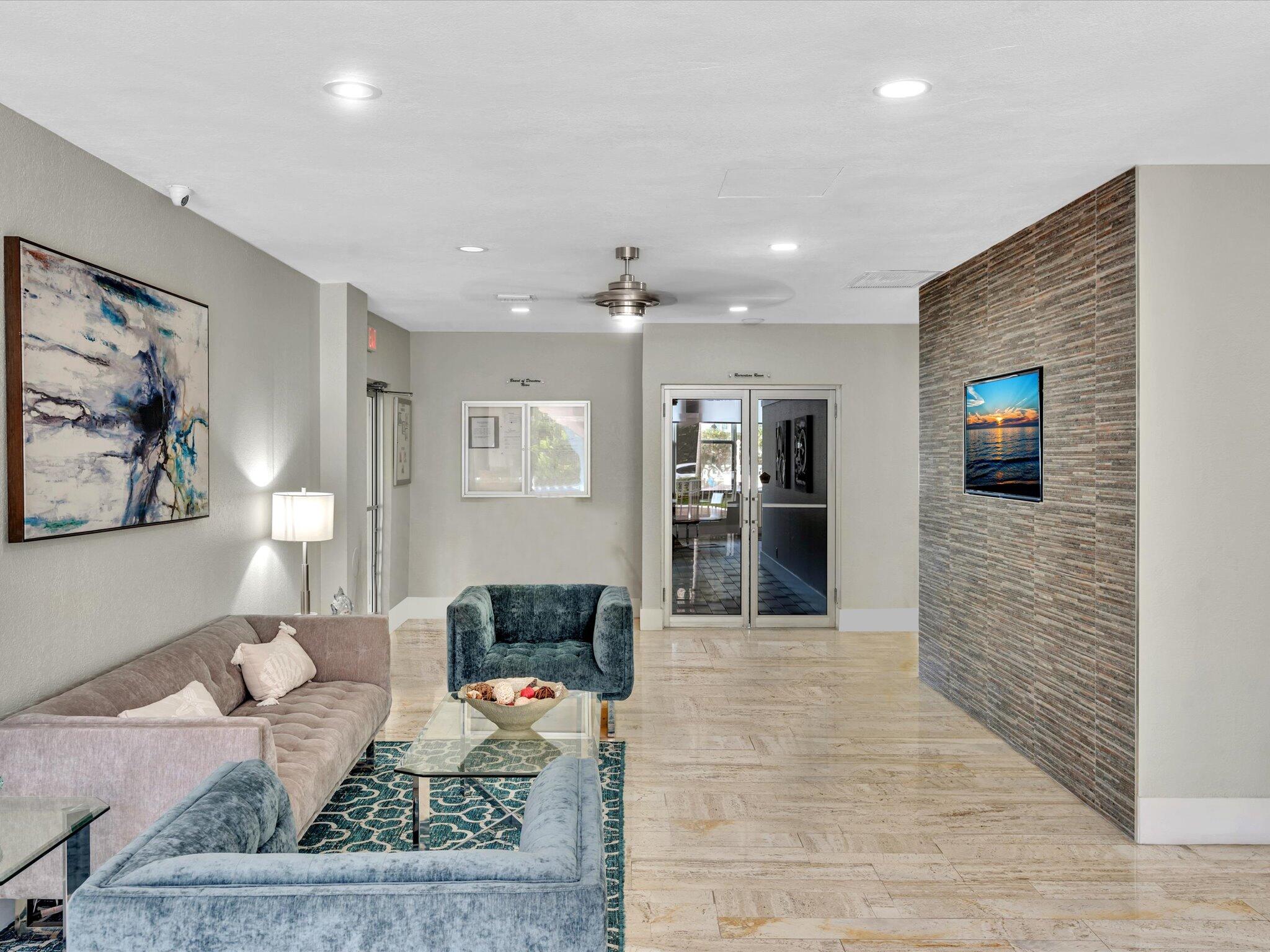 Furnished lounge with gray and blue sofas, beige tile floors, and a textured stone accent wall.