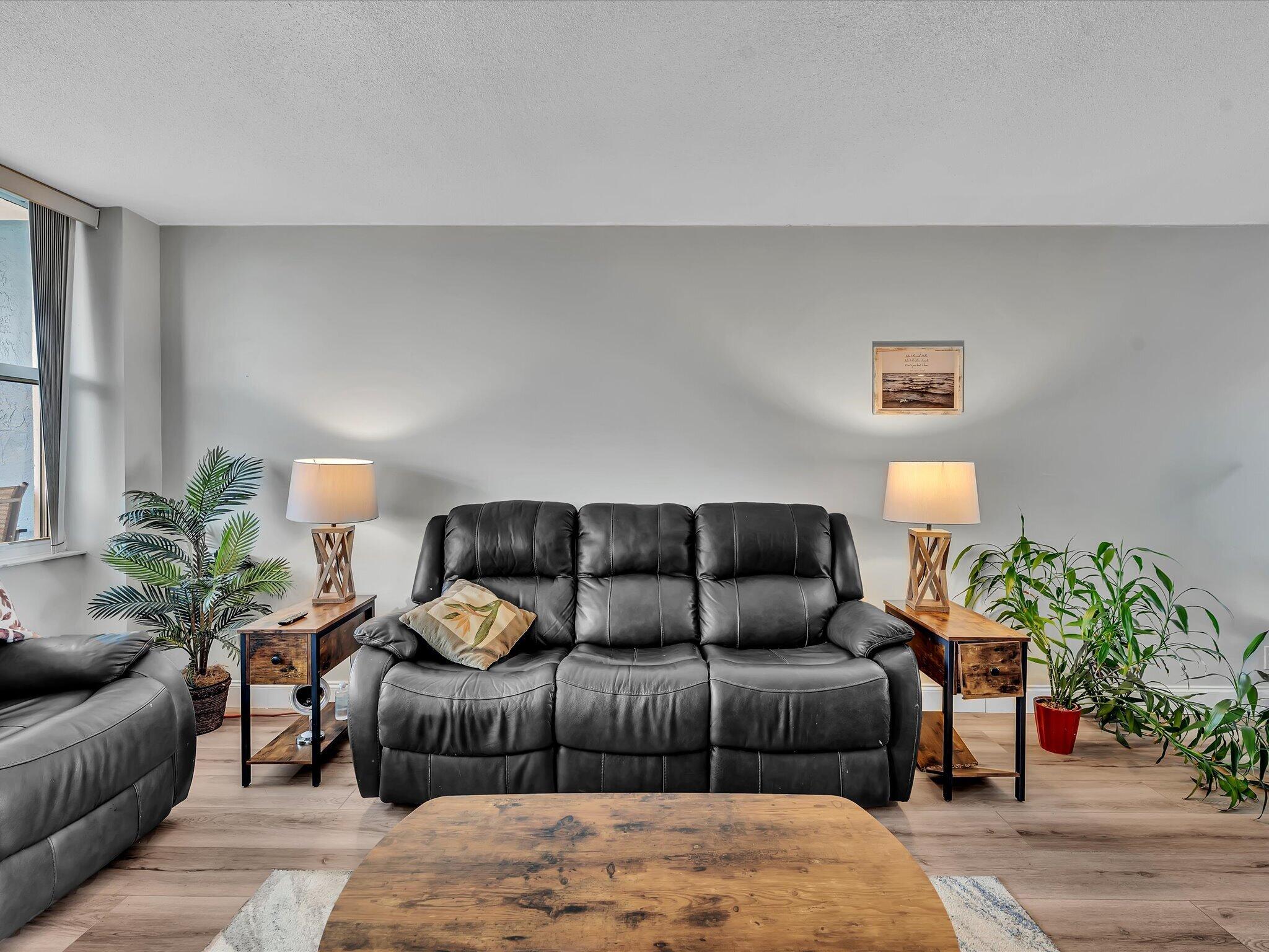 Living room with black leather sofas, wooden tables, and potted plants.