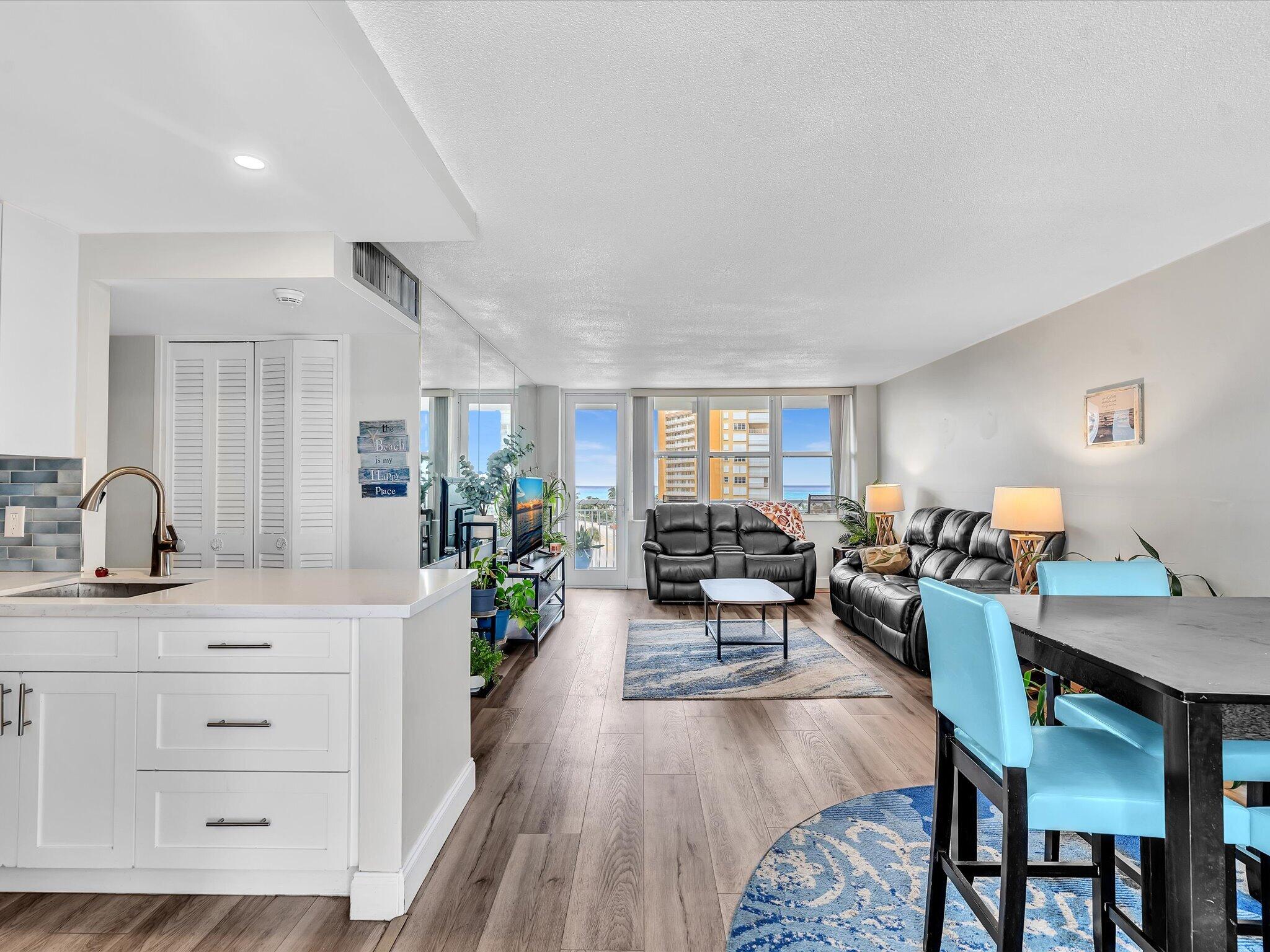 Open-plan condo living room with black leather sofas, turquoise dining chairs, and ocean views through the windows.