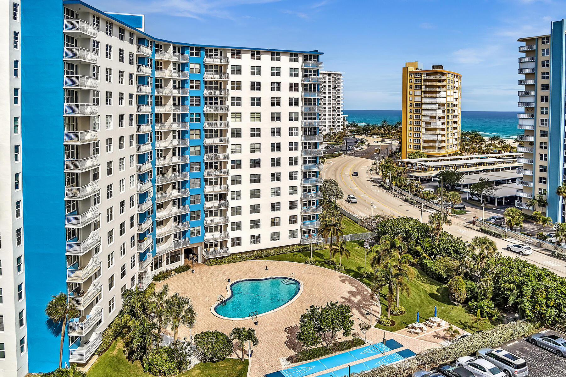 Aerial view of a blue-and-white beachfront condominium, pool, and Atlantic Ocean.