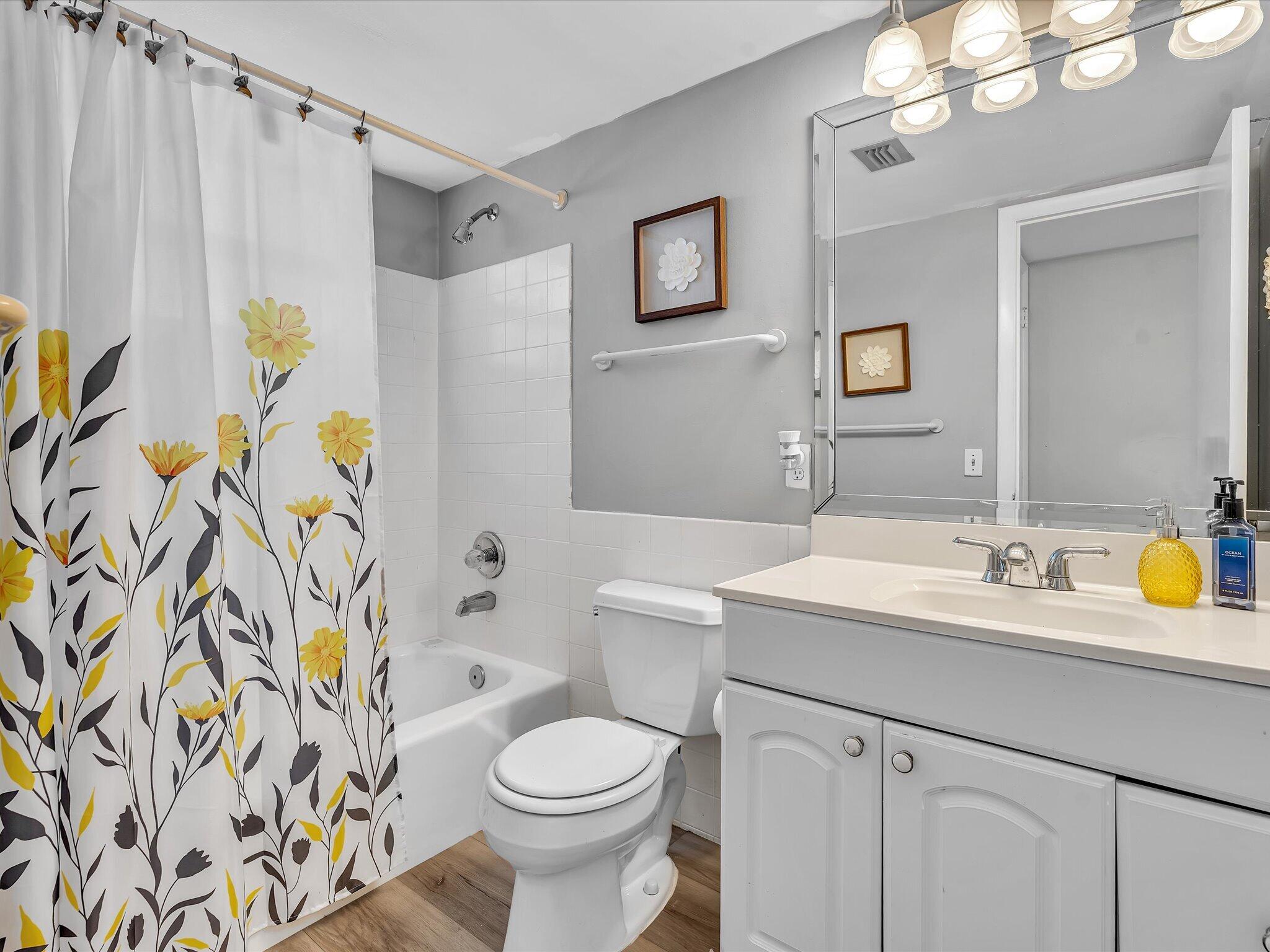 Bathroom with a floral shower curtain, white tub and toilet, and gray vanity.