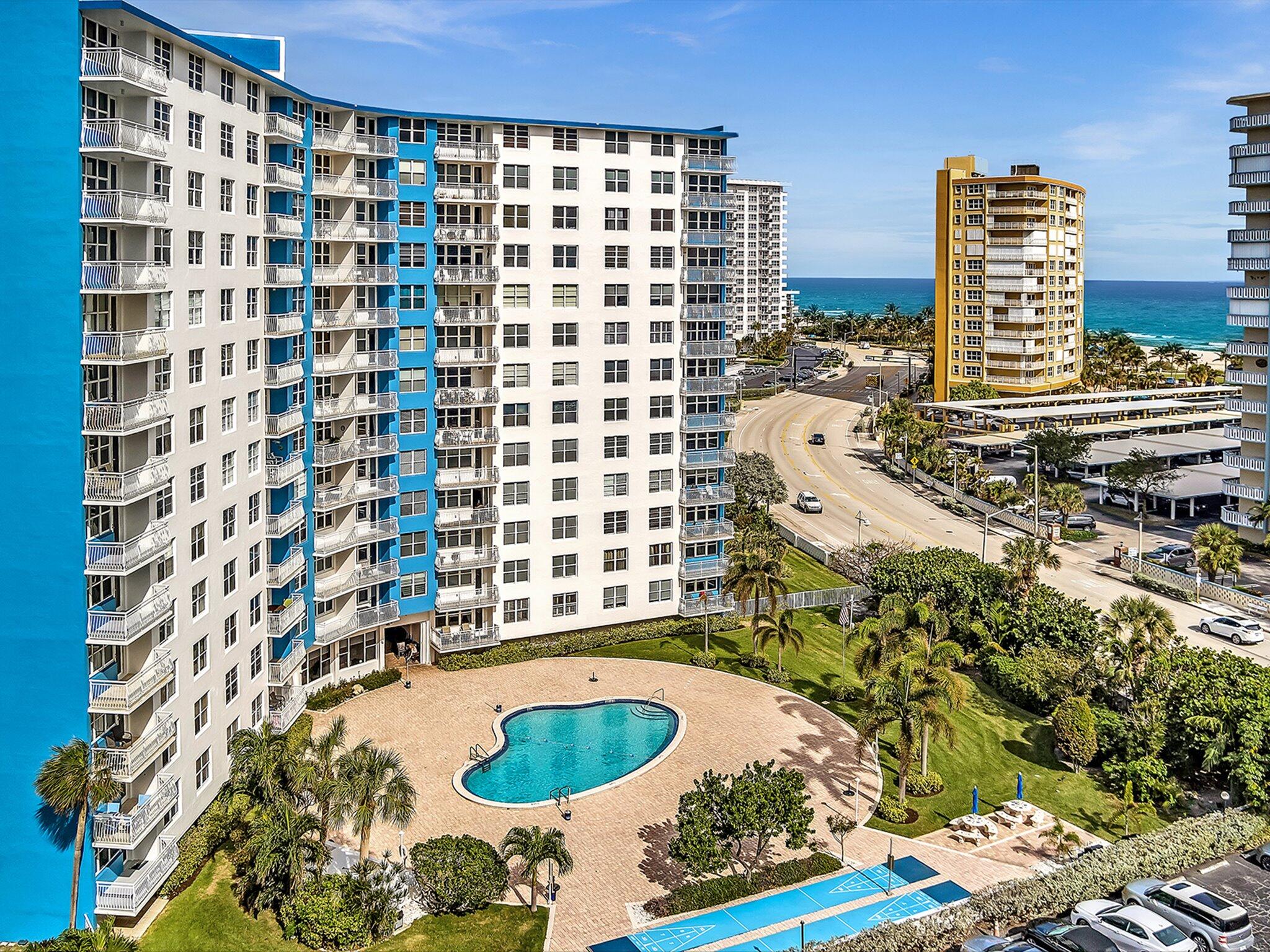 Aerial view of a beachfront condominium with a courtyard pool and ocean beyond.