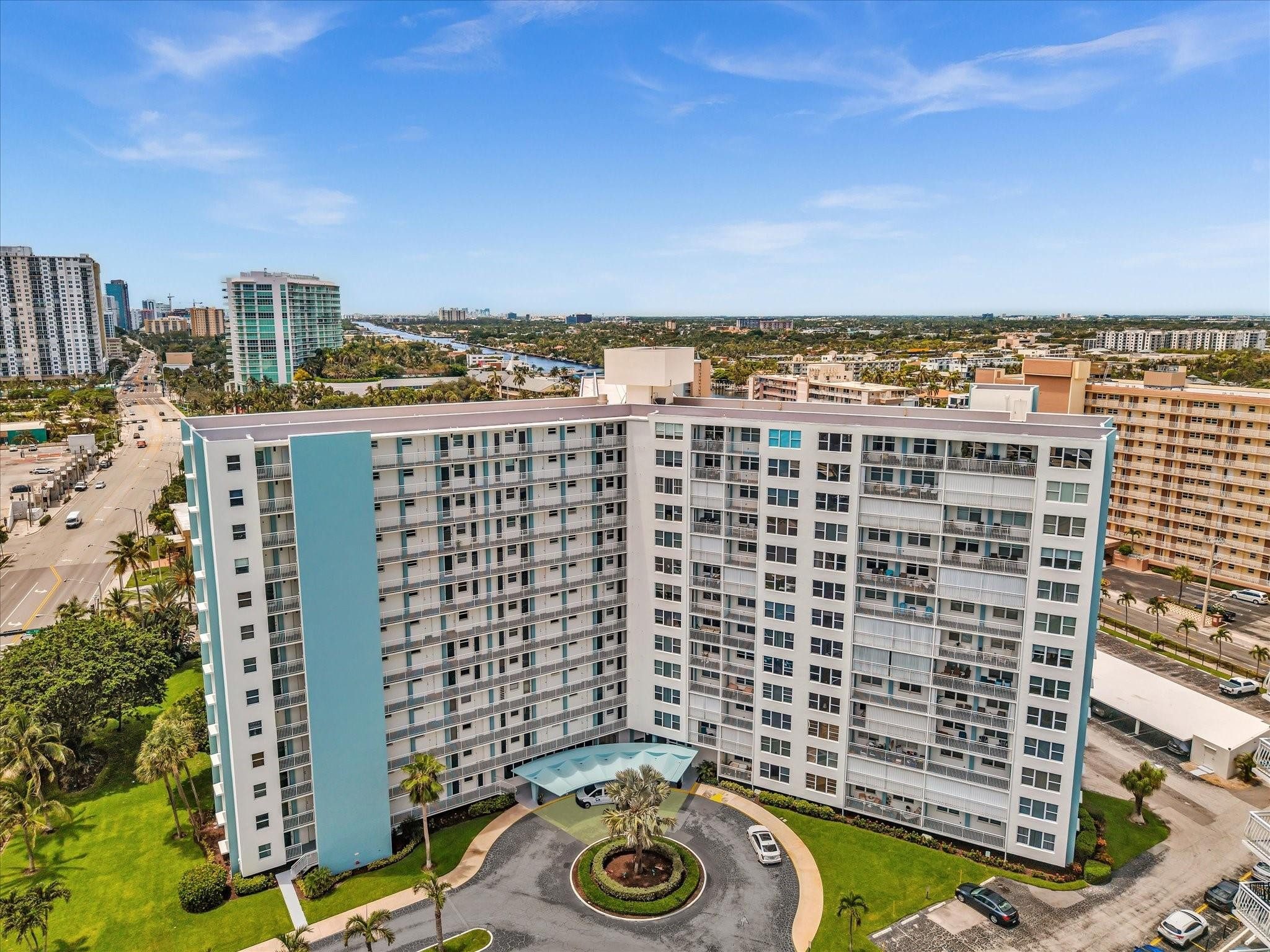 Aerial view of a white and turquoise condominium tower with balconies and a circular driveway.