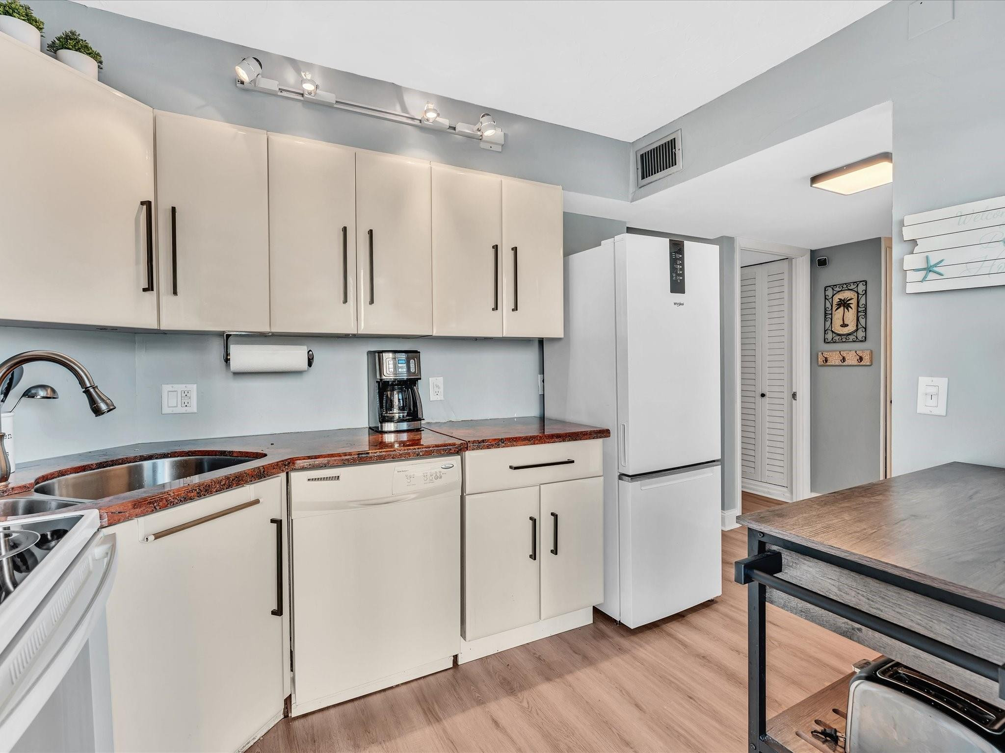 Compact kitchen with cream cabinets, reddish countertops, and a white refrigerator.