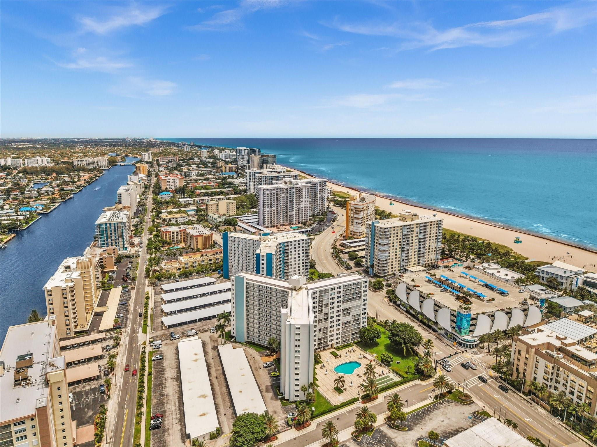Aerial view of beachfront high-rises, sandy shore, ocean, and a canal.