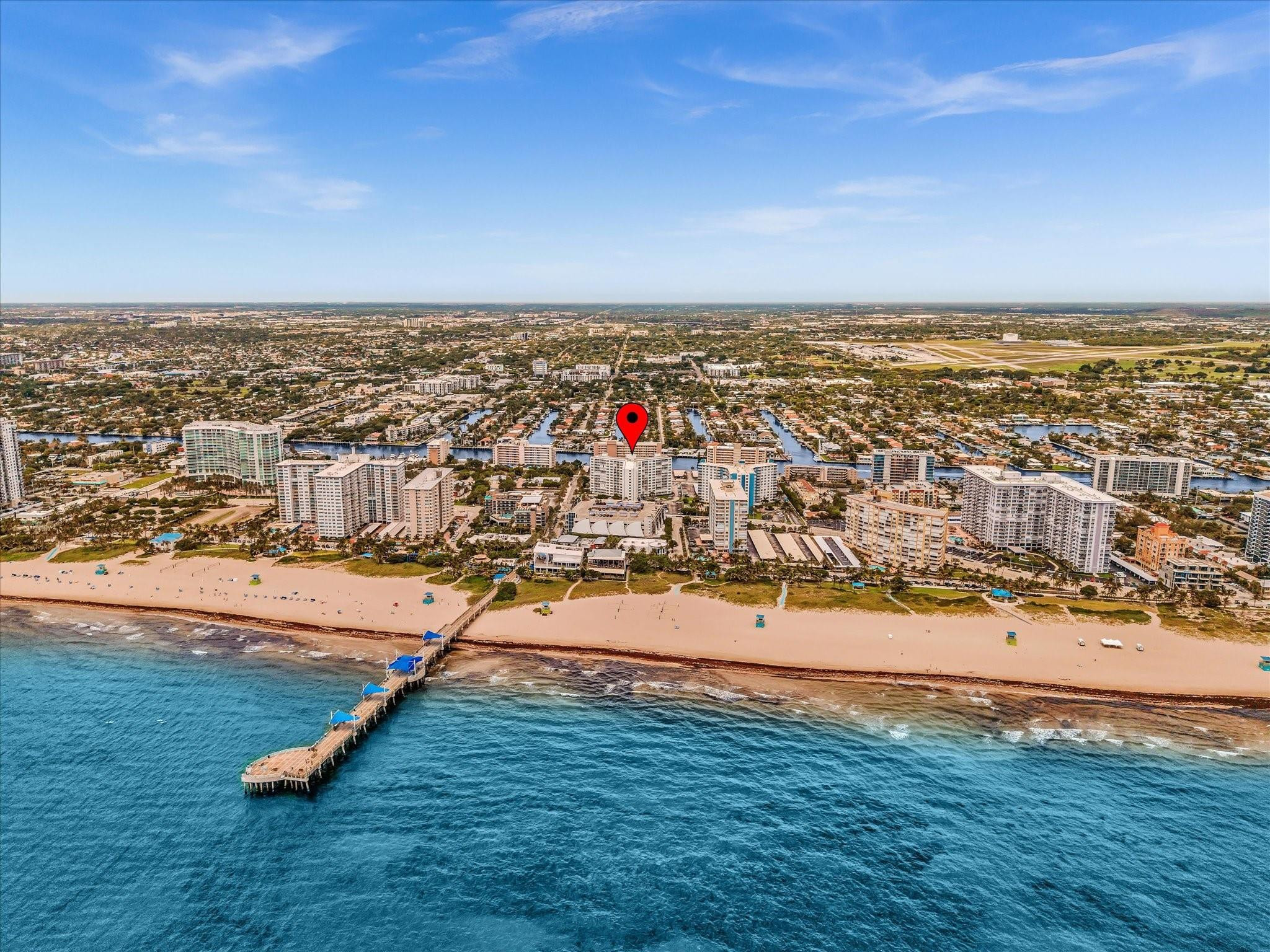 Aerial beachfront view with a red pin marking a coastal condominium beside the beach and pier.