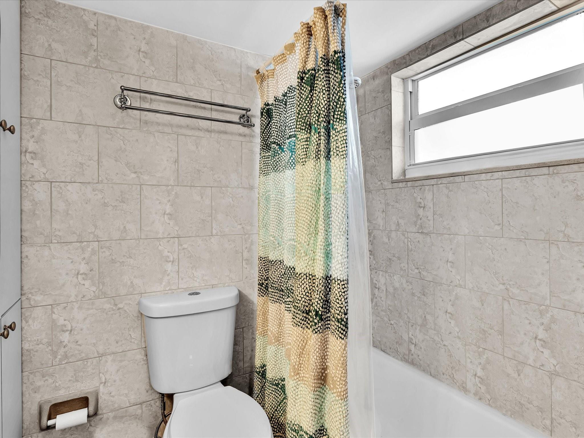 Bathroom with tiled walls, a patterned shower curtain, bathtub, and high window.