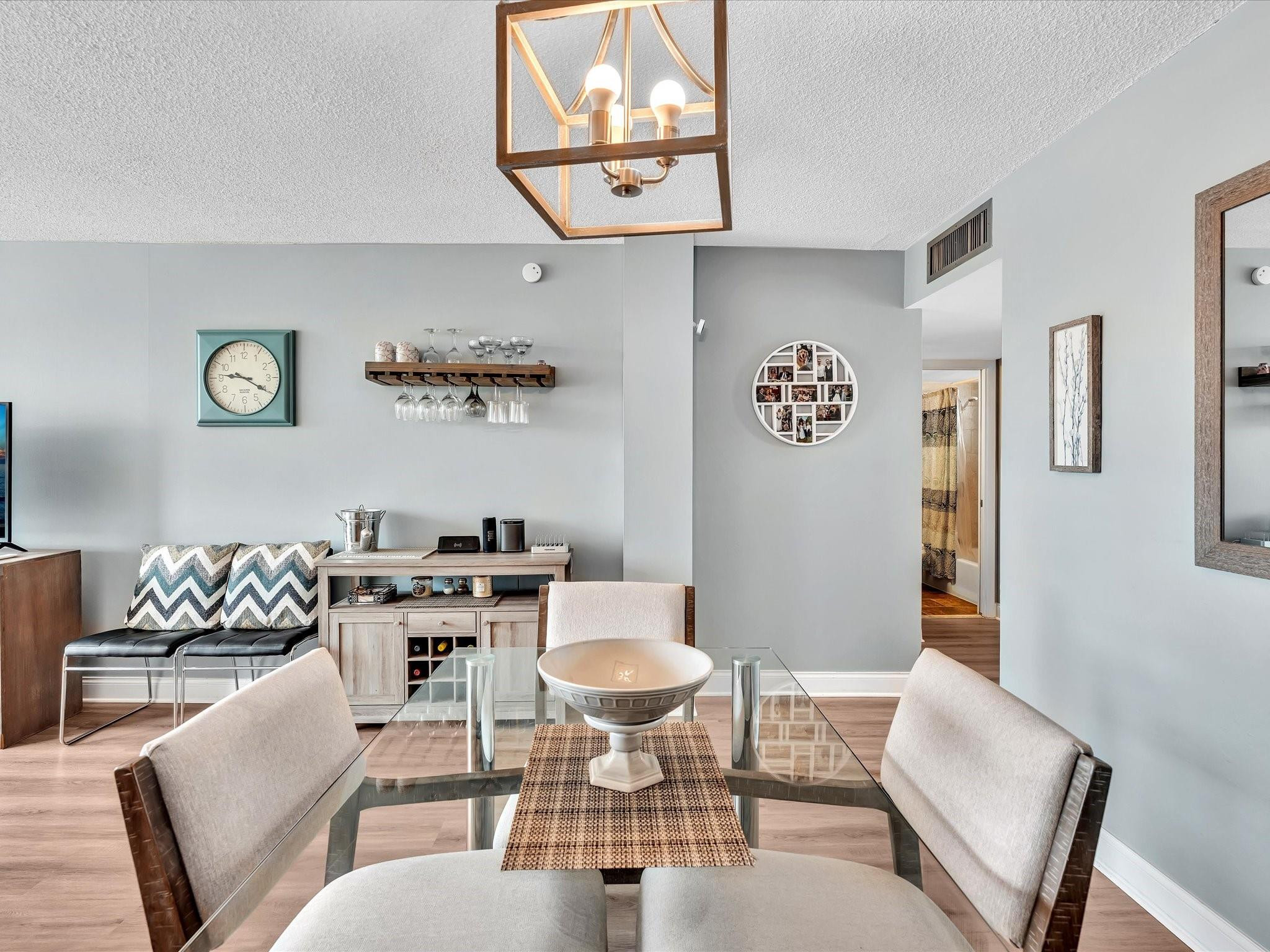 Furnished dining area with a glass table, upholstered chairs, and a wall-mounted stemware rack.