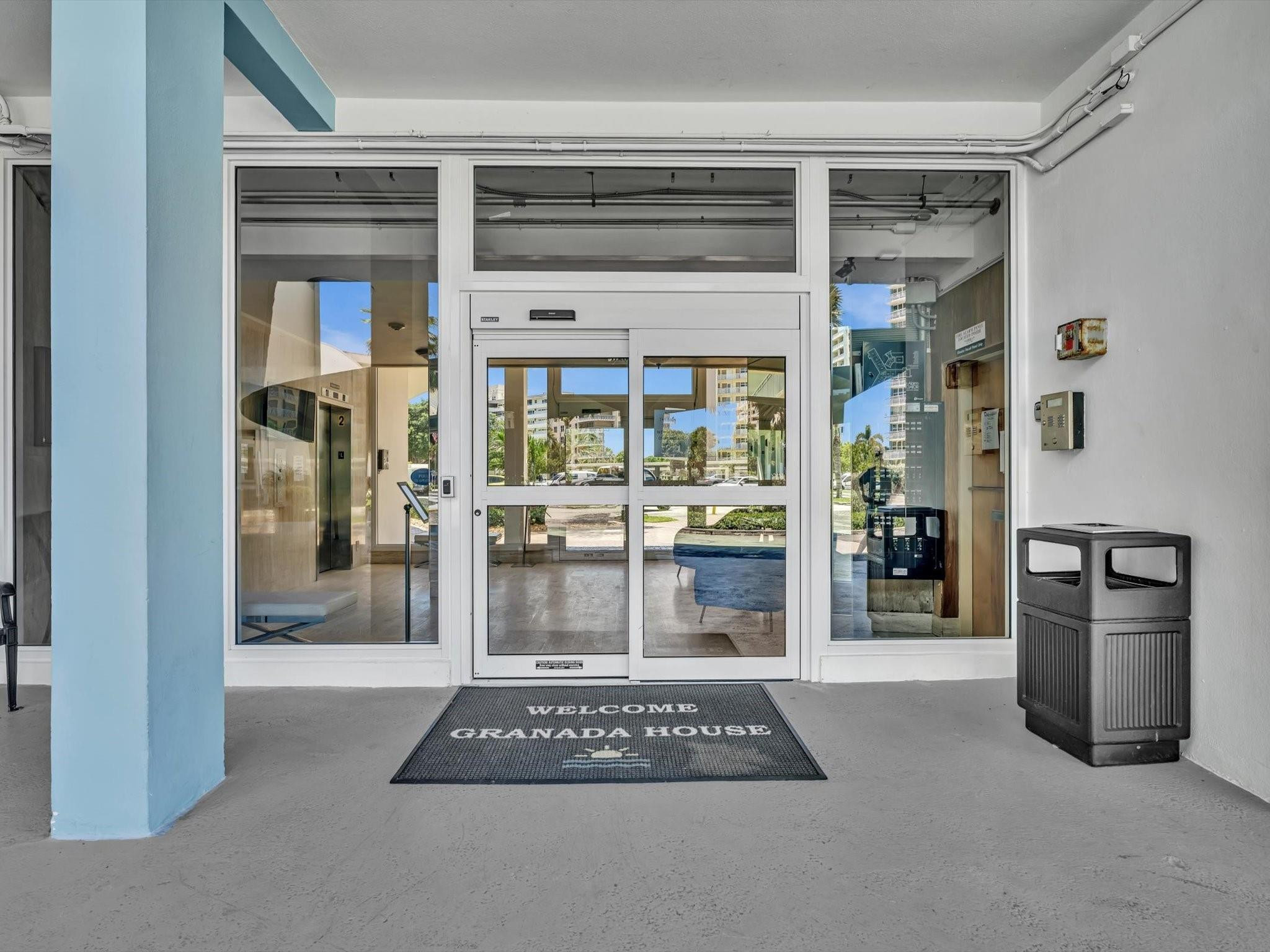 Granada House condominium entrance with glass doors, a blue column, and a welcome mat.