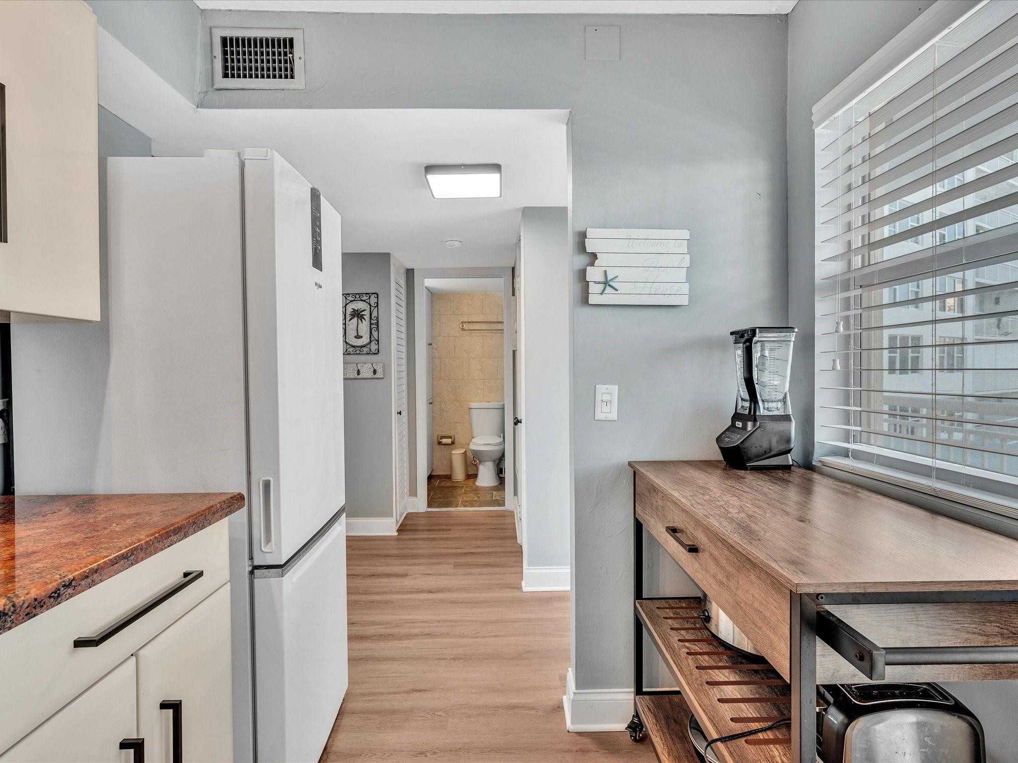 Condo kitchen with a wood island and blender, white refrigerator, and bathroom visible through the doorway.