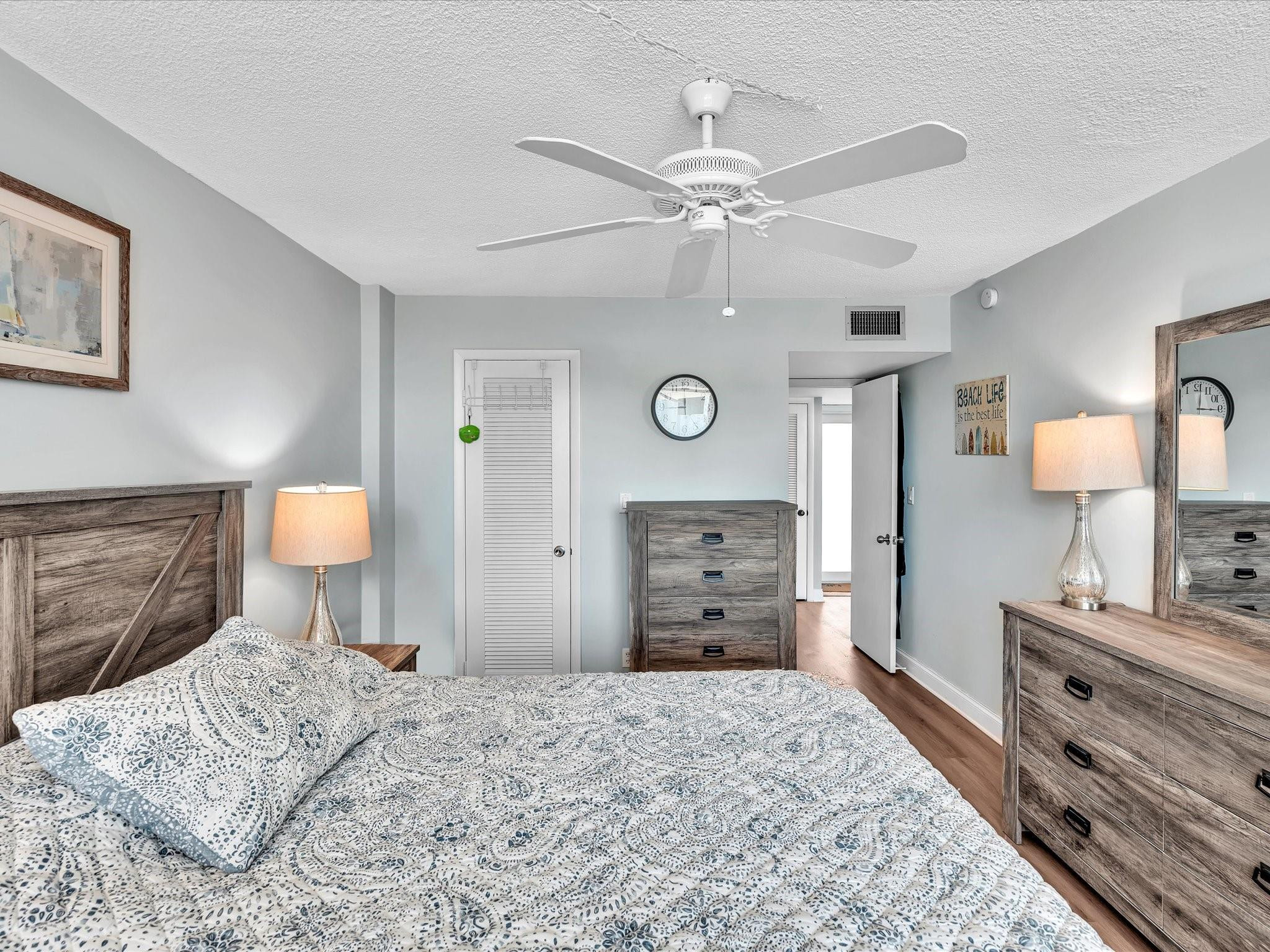 Furnished bedroom with patterned bedding, gray wood furniture, and a white ceiling fan.