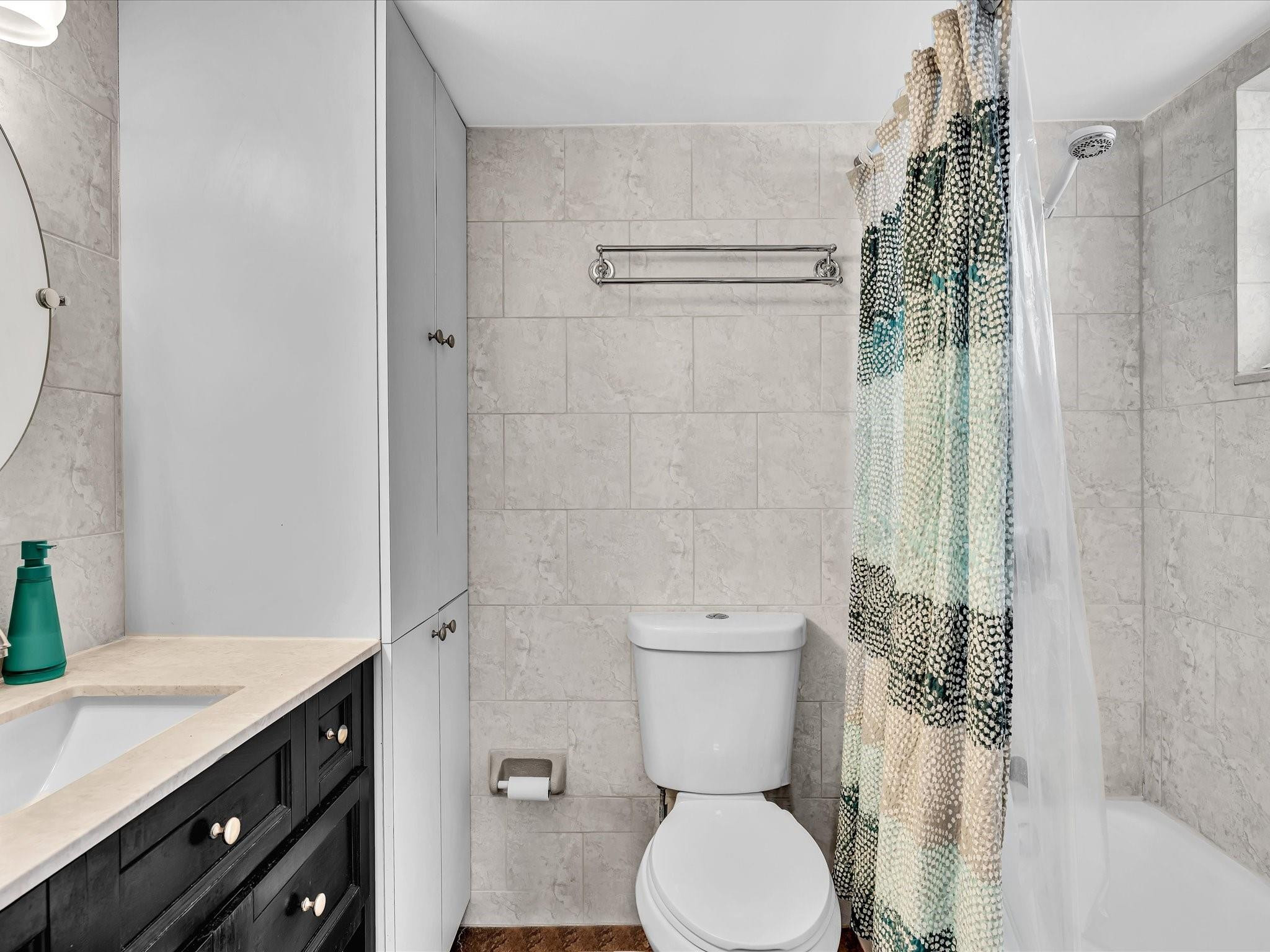 Bathroom with tiled walls, a dark vanity, and a bathtub behind a patterned shower curtain.