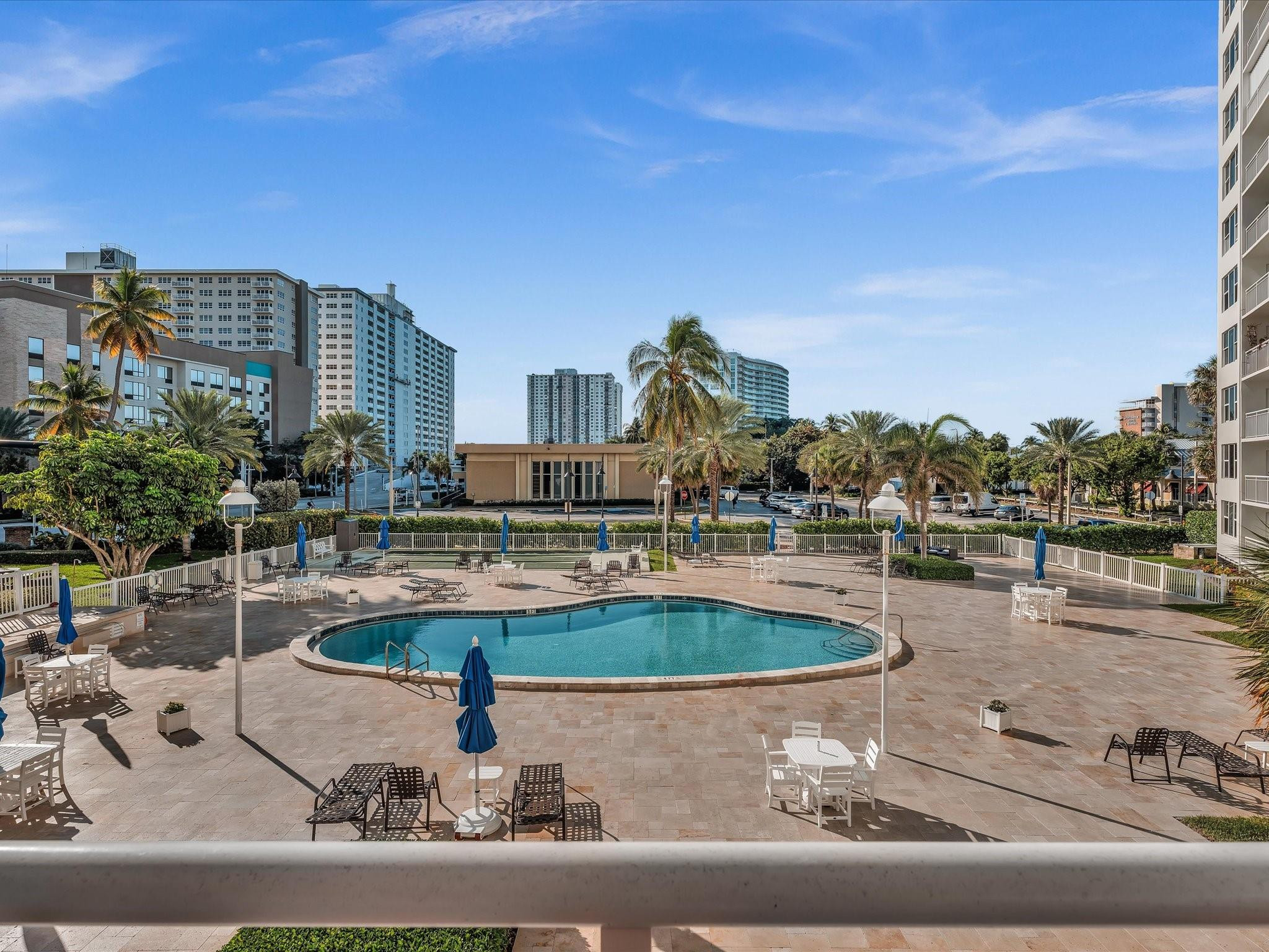 Condominium pool deck with palm trees, lounge chairs, and nearby high-rise buildings.