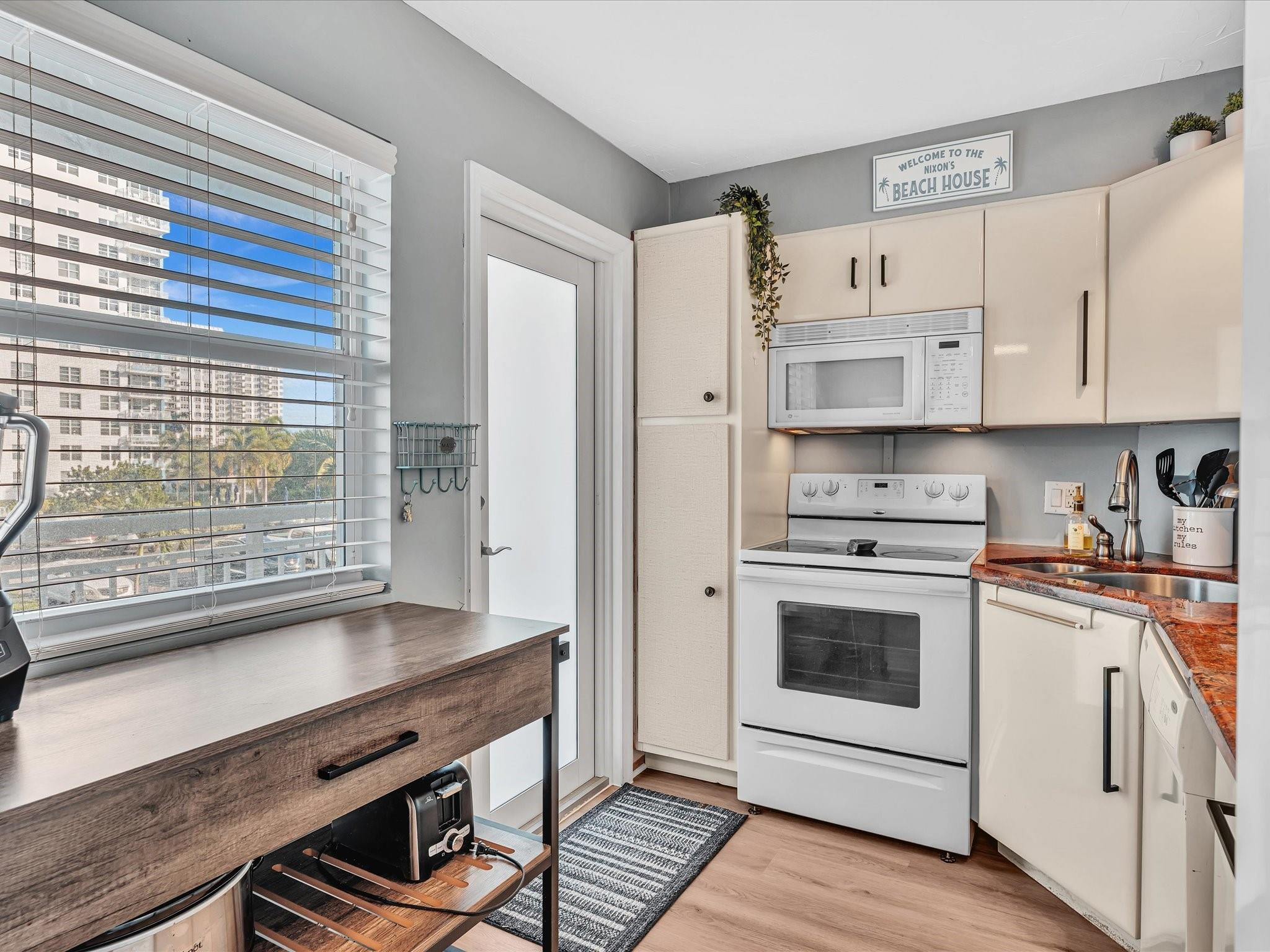Condominium kitchen with white appliances, reddish stone counters, and a window overlooking neighboring high-rises.