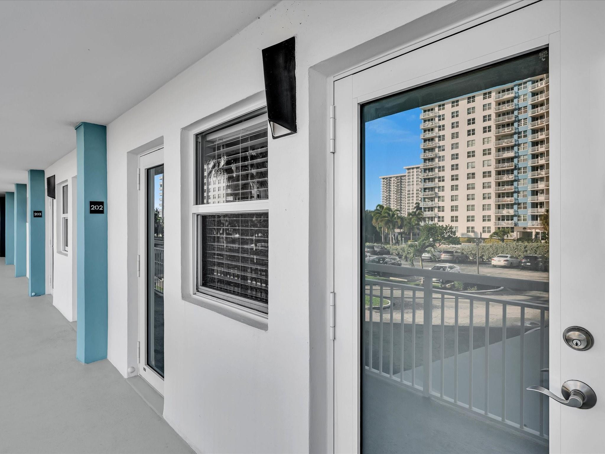 Condominium exterior corridor with turquoise columns and unit 202’s glass door overlooking neighboring towers.