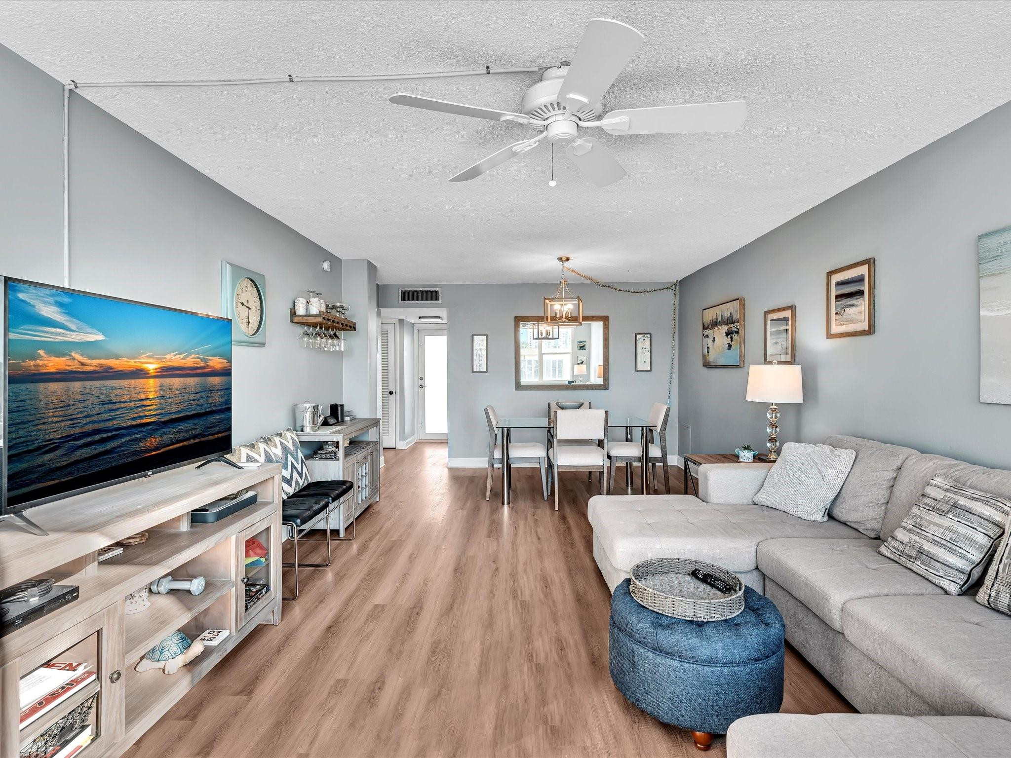 Open-plan living and dining room with a gray sectional, large television, and wood-look floors.
