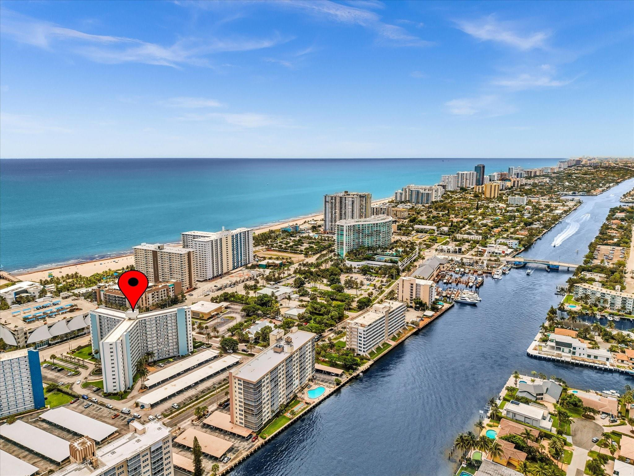 Aerial view of beachfront high-rises and marina, with a red marker identifying the property.