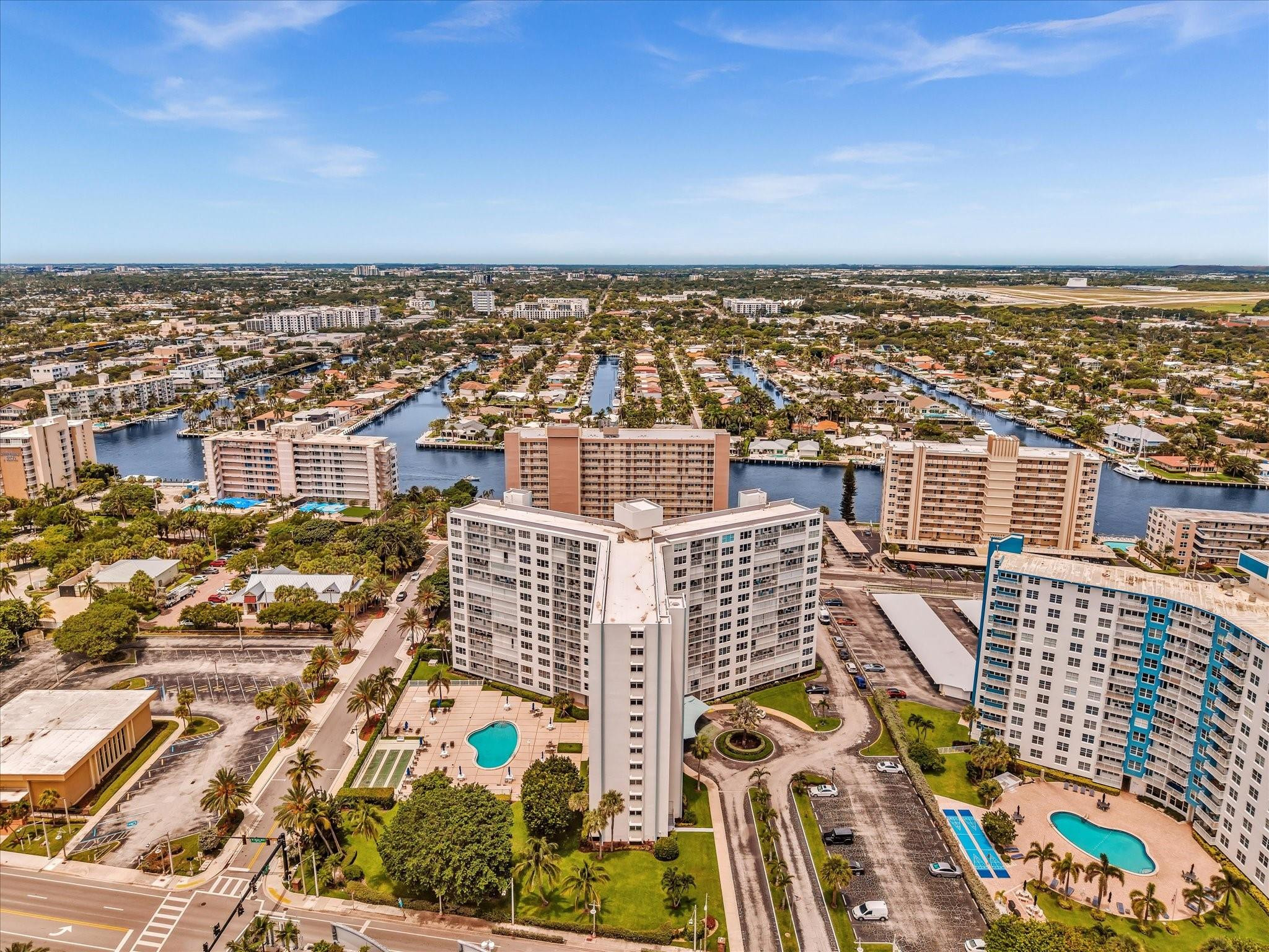 Aerial view of a white condominium complex with pools, palm trees, and canals nearby.