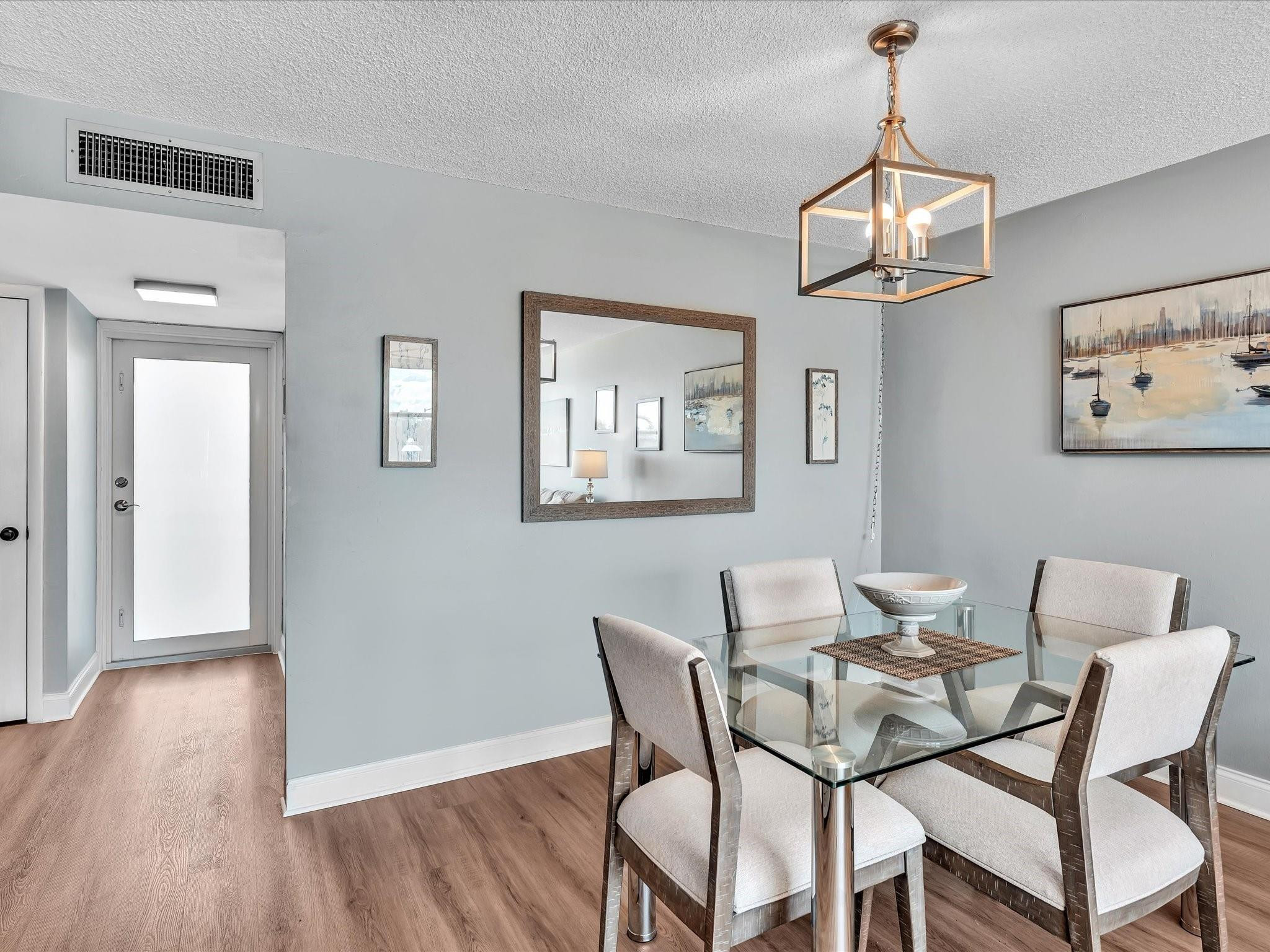 Dining area with a glass-top table, four upholstered chairs, and a geometric pendant light.