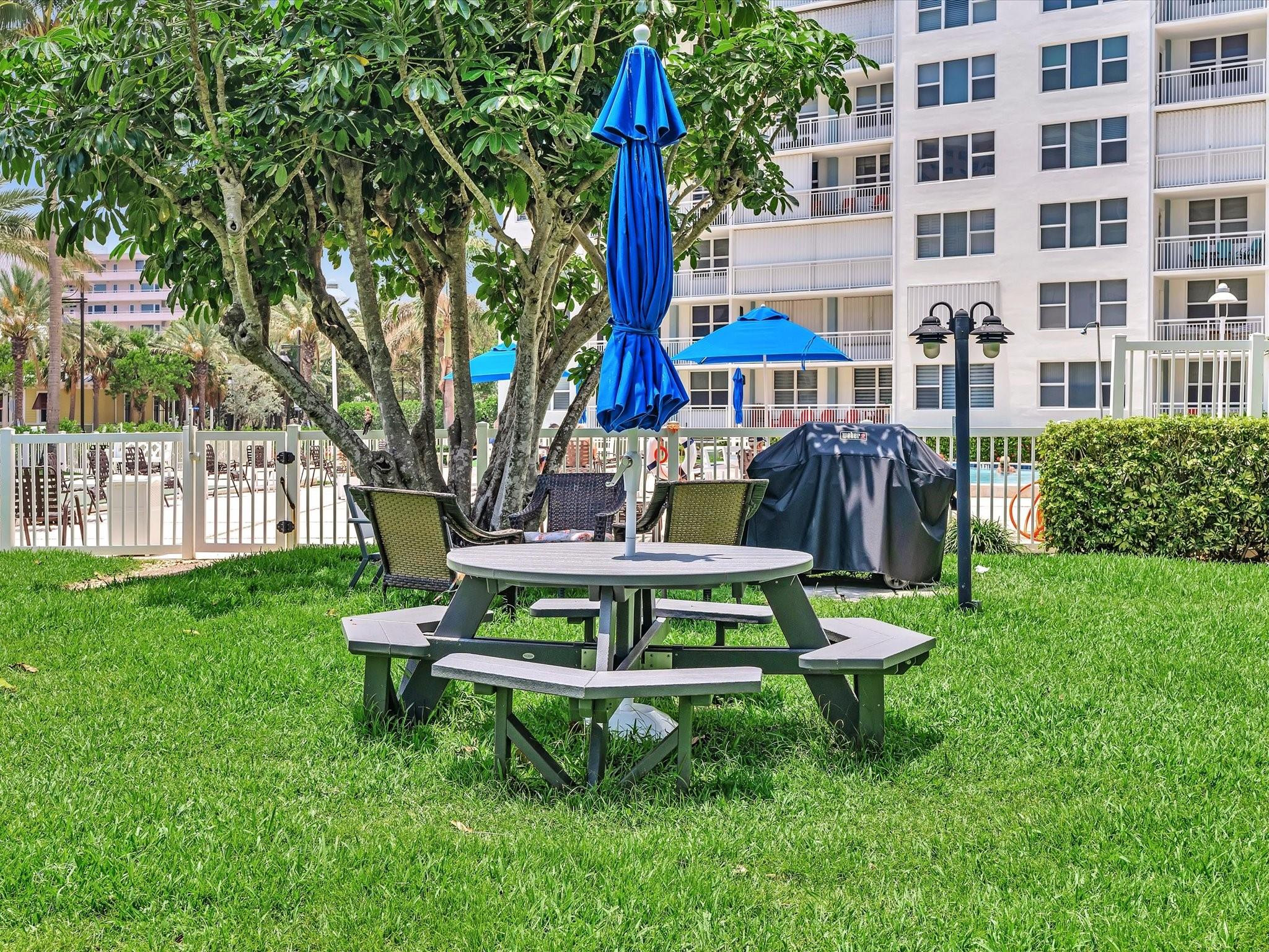 Condominium courtyard with picnic table, blue umbrellas, pool, and lawn.