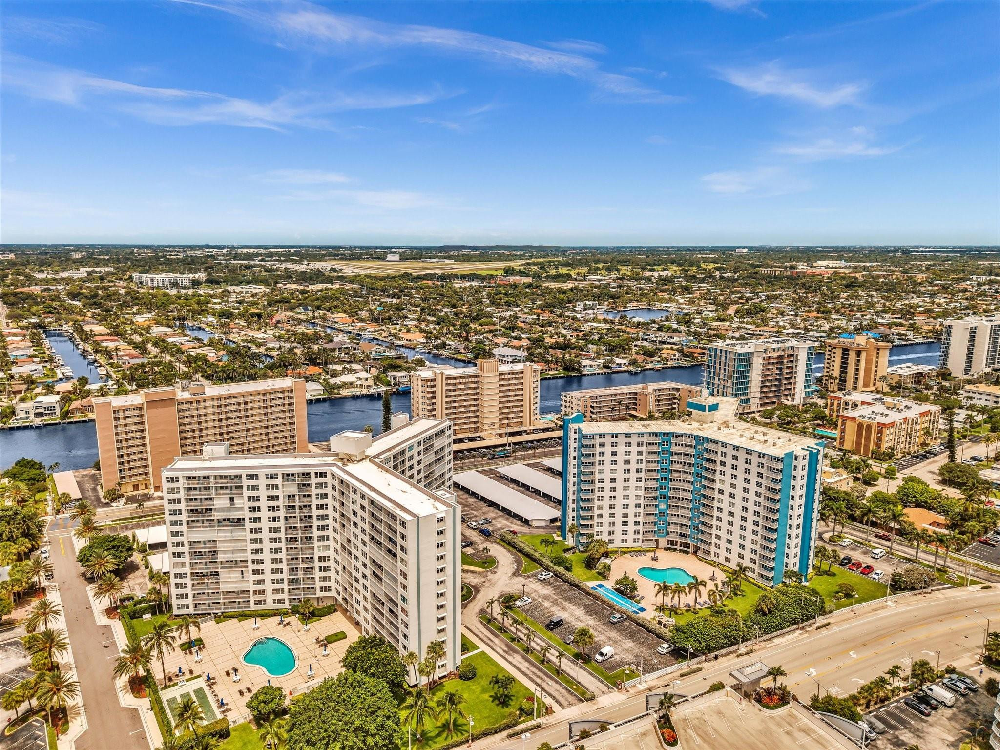 Aerial view of condominium buildings and pools beside a canal and coastal boulevard.