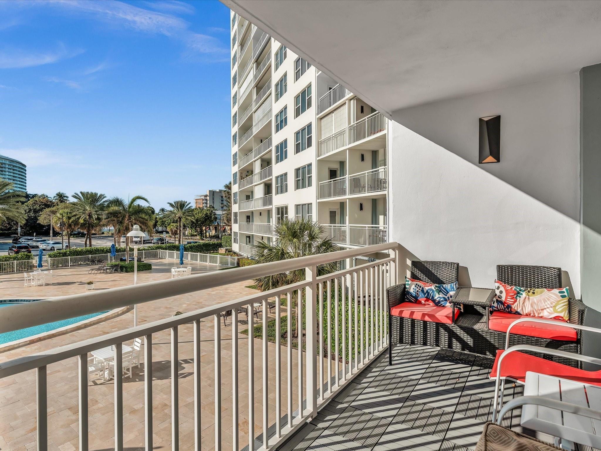 Condo balcony with colorful wicker seating overlooking a pool deck and palm trees.