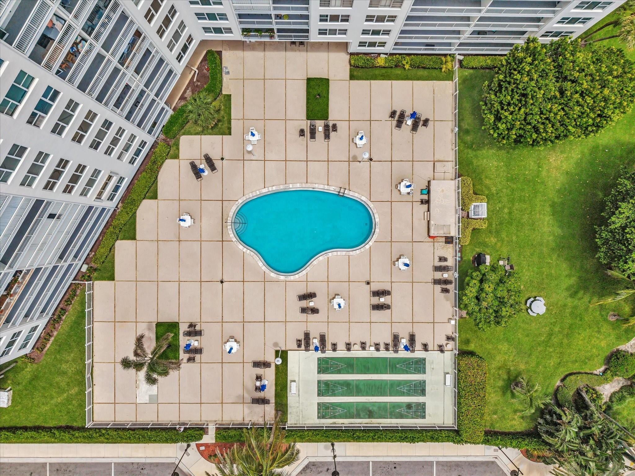 Aerial view of a condominium pool deck with lounge chairs, landscaped grounds, and three courts.