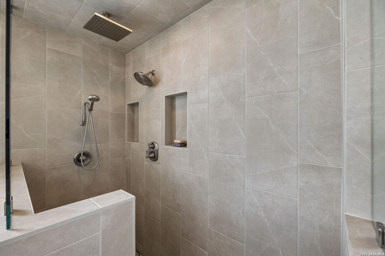 Walk-in shower with large stone-look tiles, a rain showerhead, handheld sprayer, and two recessed niches.