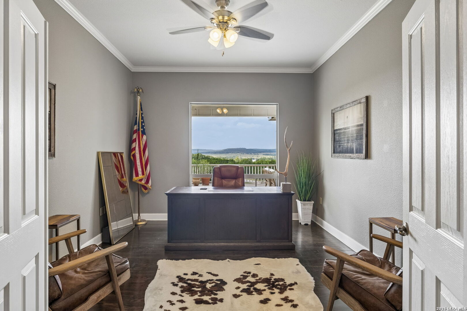 Furnished home office with a dark desk, leather chairs, and a wide view of rolling hills.