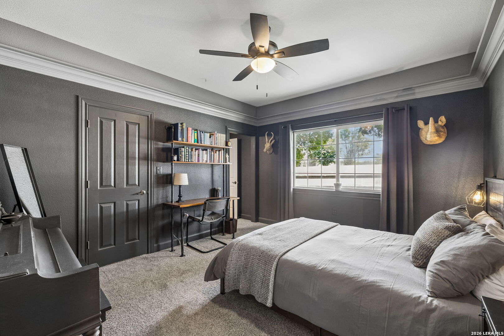 Bedroom with gray bedding, dark walls, a desk and bookshelves beside a large window.
