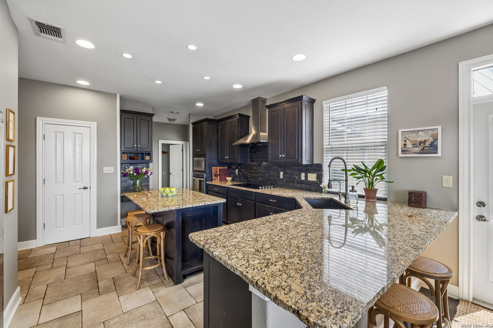Kitchen with dark wood cabinets, granite counters, a large peninsula, and bar stools.