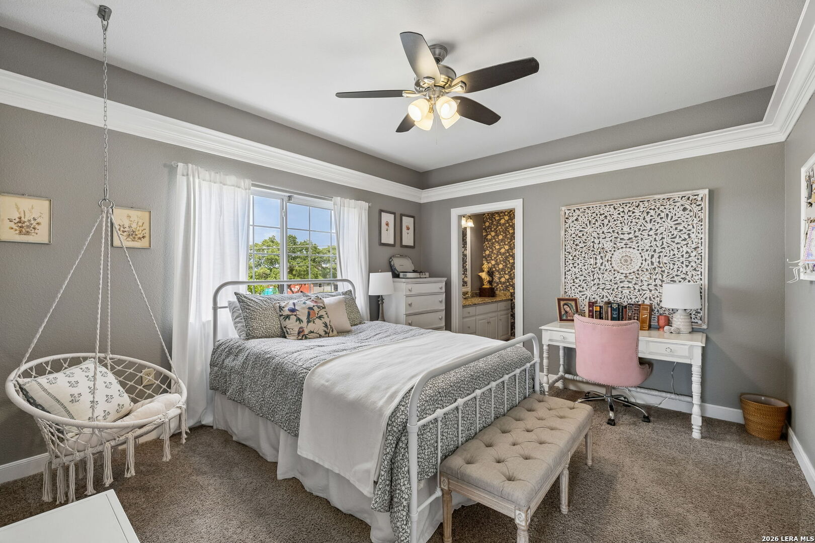 Bedroom with a white metal bed, hanging wicker chair, and desk with a pink chair.