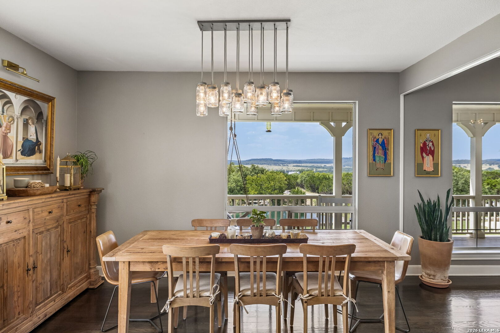Dining room with a wooden table, jar chandelier, and windows overlooking green hills.