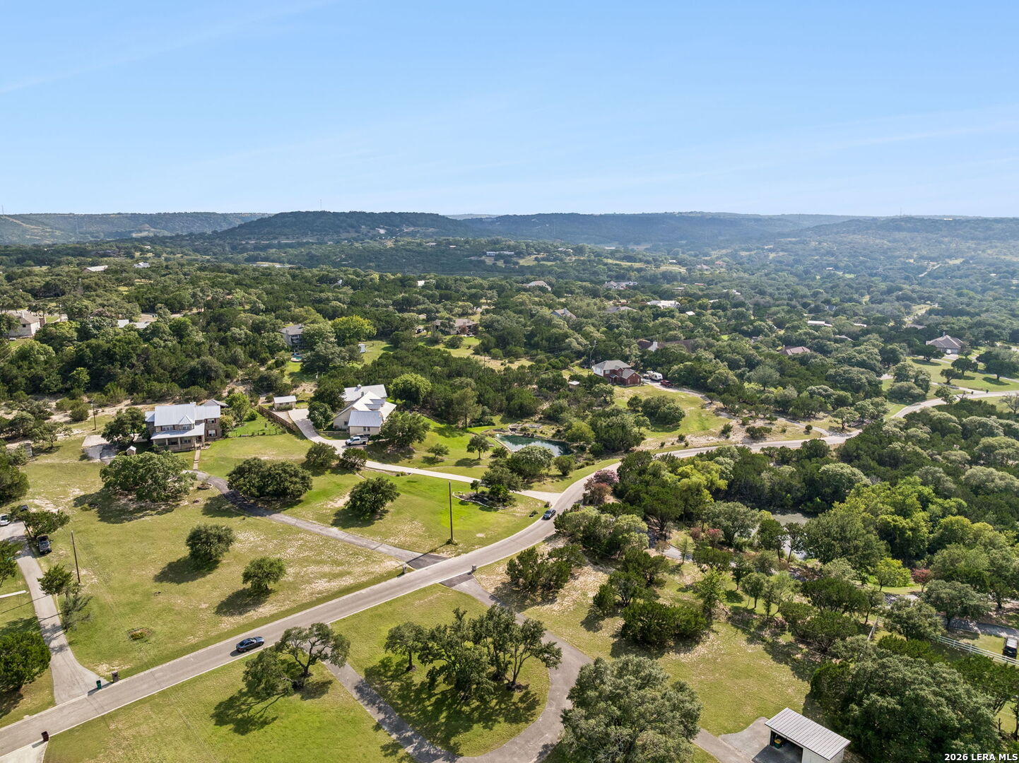 Aerial view of spacious homesites along a winding road amid trees and rolling hills.