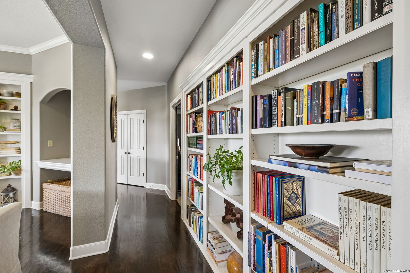 Hallway lined with white built-in bookshelves filled with books and decor.