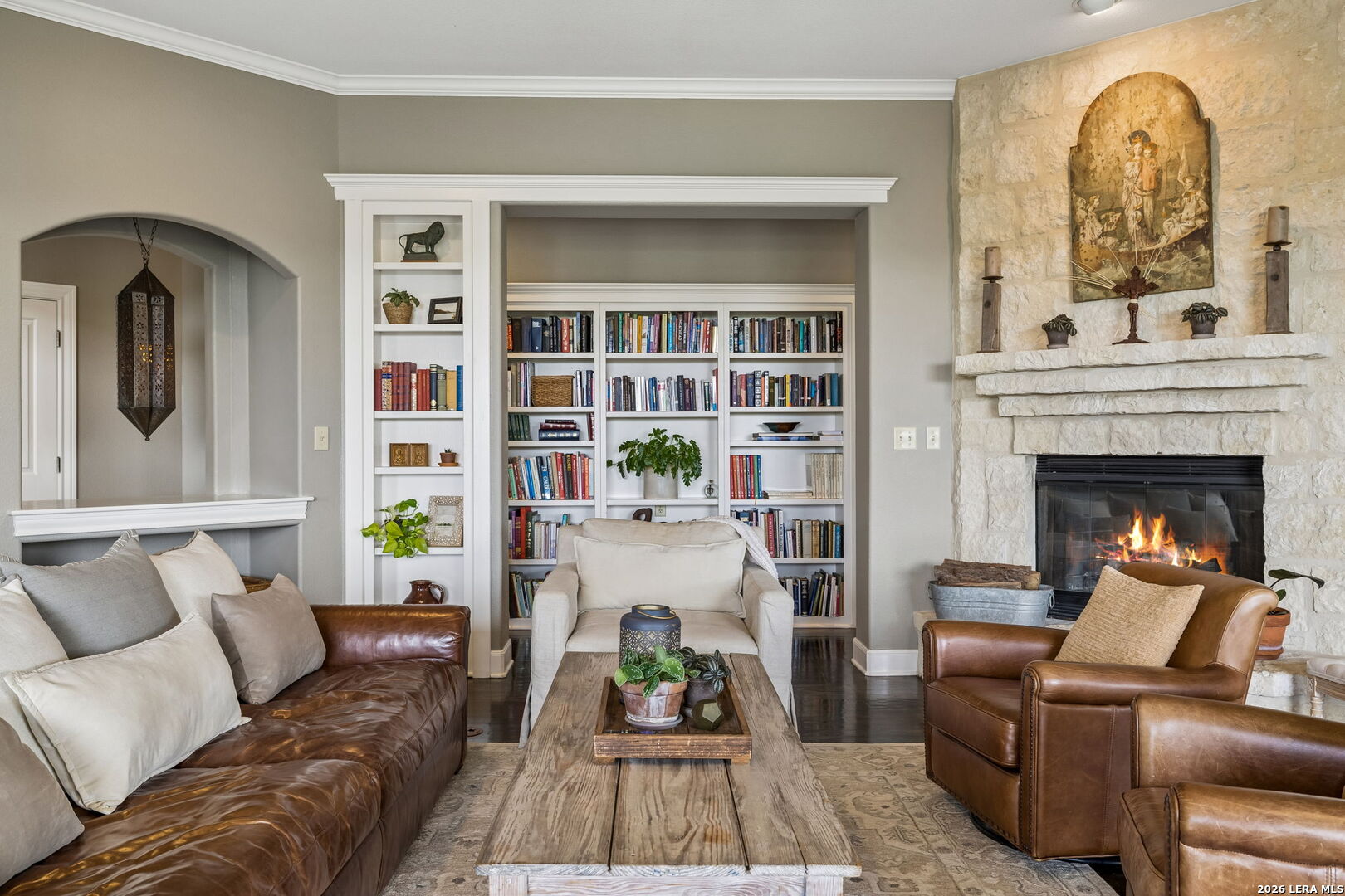 Living room with built-in bookshelves, leather seating, and a lit stone fireplace.