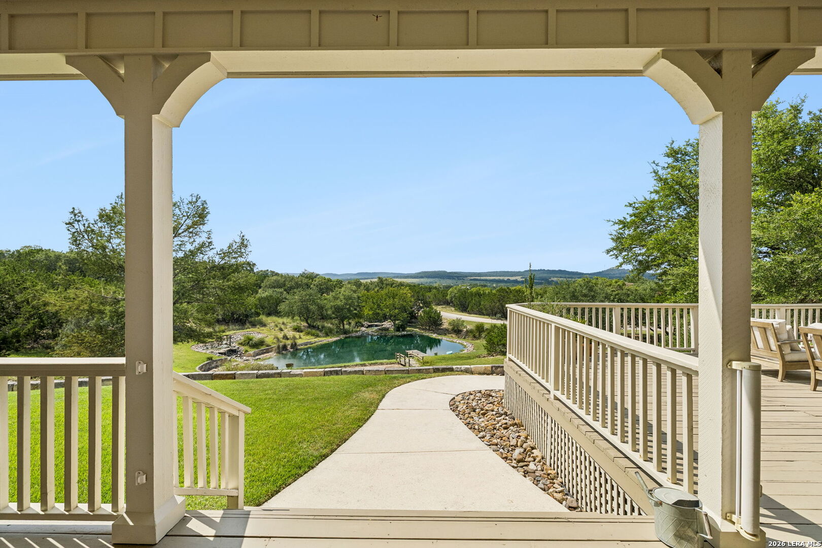 Covered porch overlooking a landscaped pond, wooded hills, and a curved walkway.