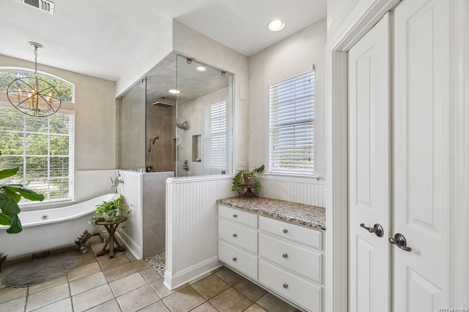 Bathroom with a freestanding tub, glass-enclosed tiled shower, and white vanity with granite countertop.