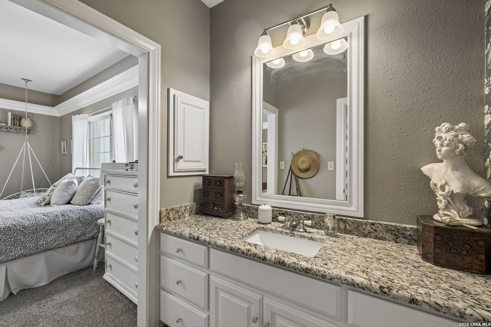 Bathroom vanity with granite countertop and large mirror, overlooking an adjoining bedroom.