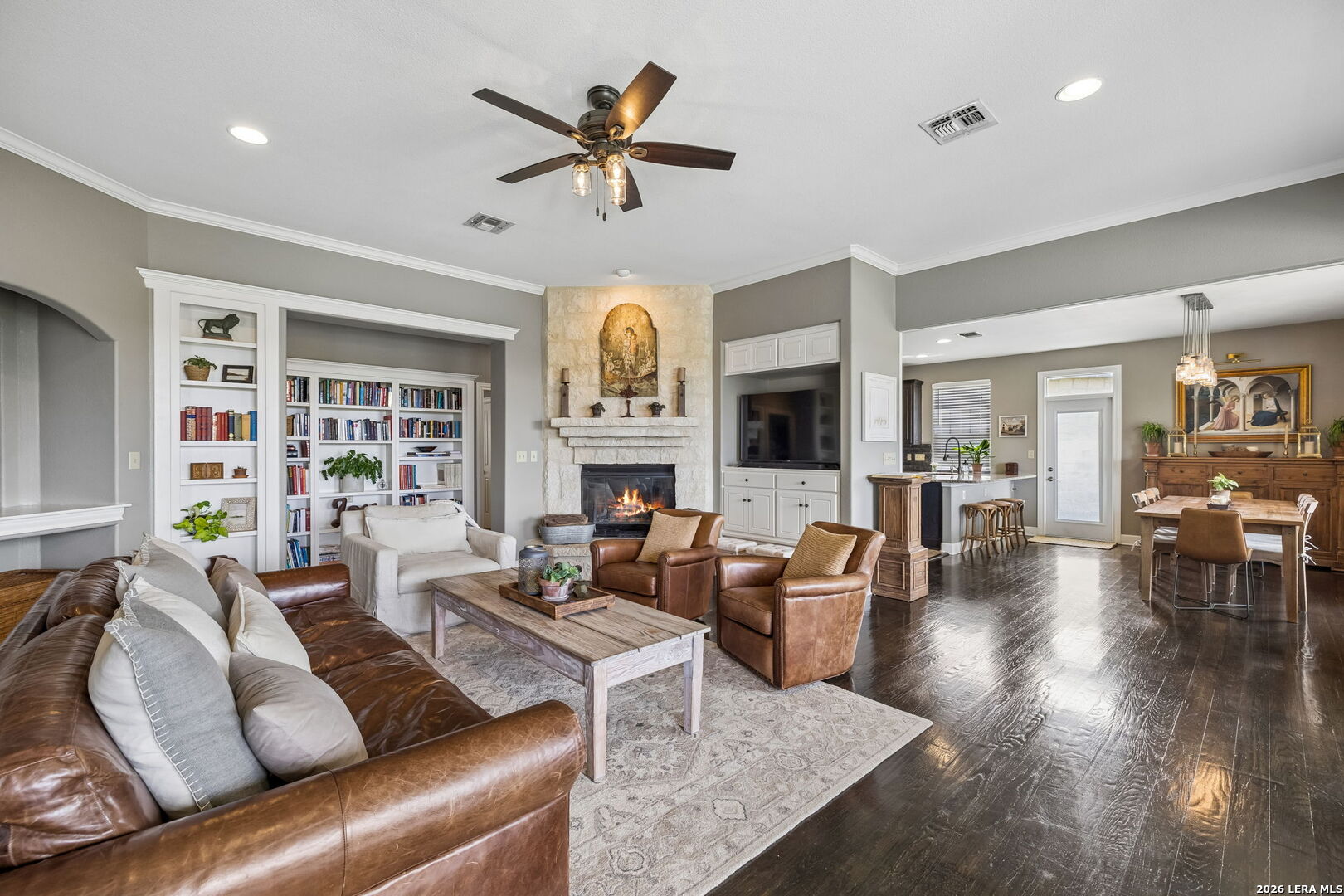 Living room with stone fireplace, built-in bookshelves, leather seating, and an adjoining dining area.